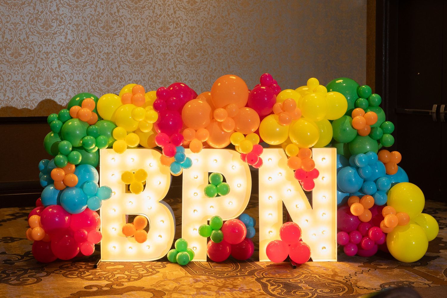 Colorful balloon arch with illuminated 'BPN' letters in white against a dark background.