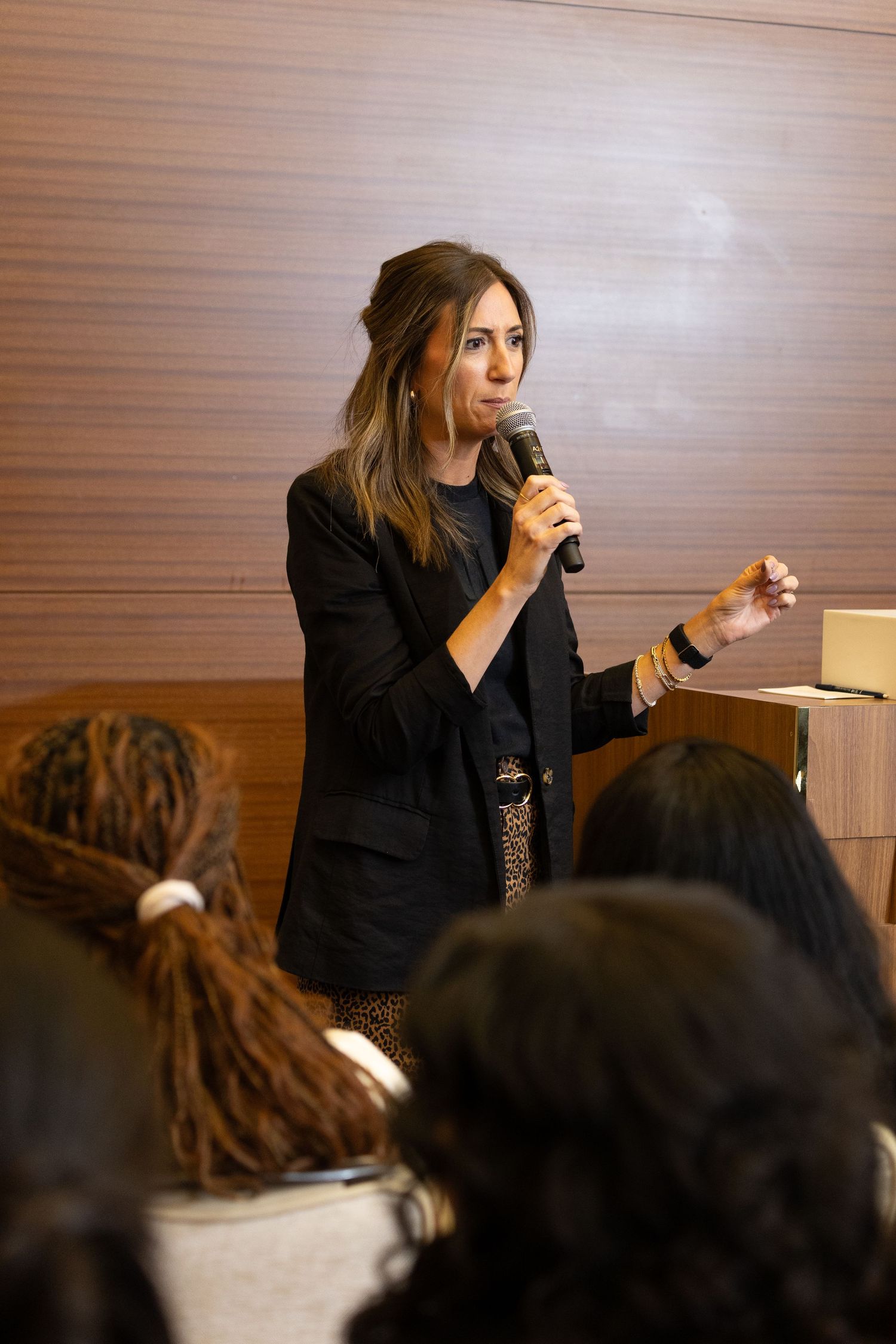 Speaker presenting to audience in conference room with wood paneled walls.