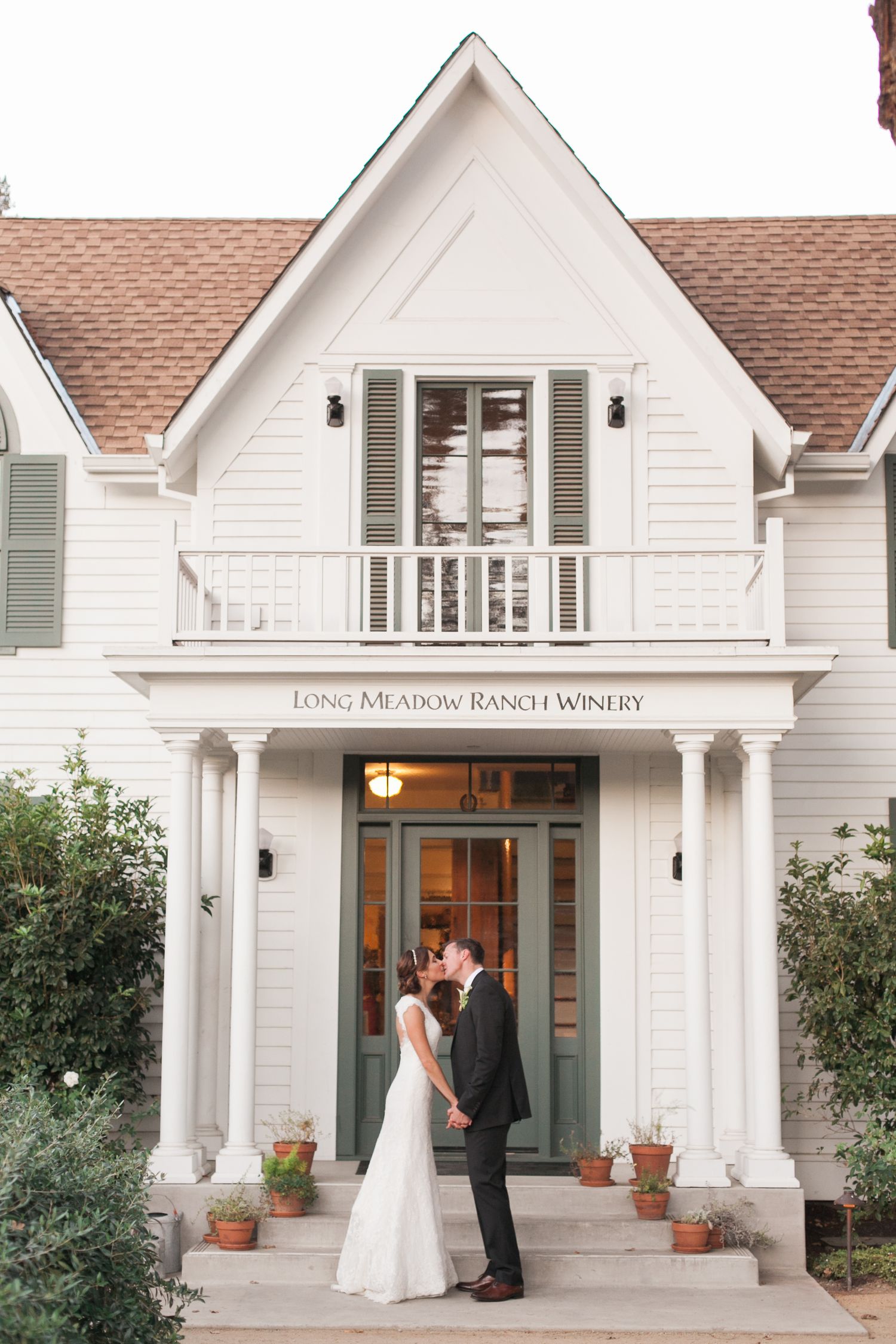 White farmhouse-style winery entrance with wedding couple on the front porch.