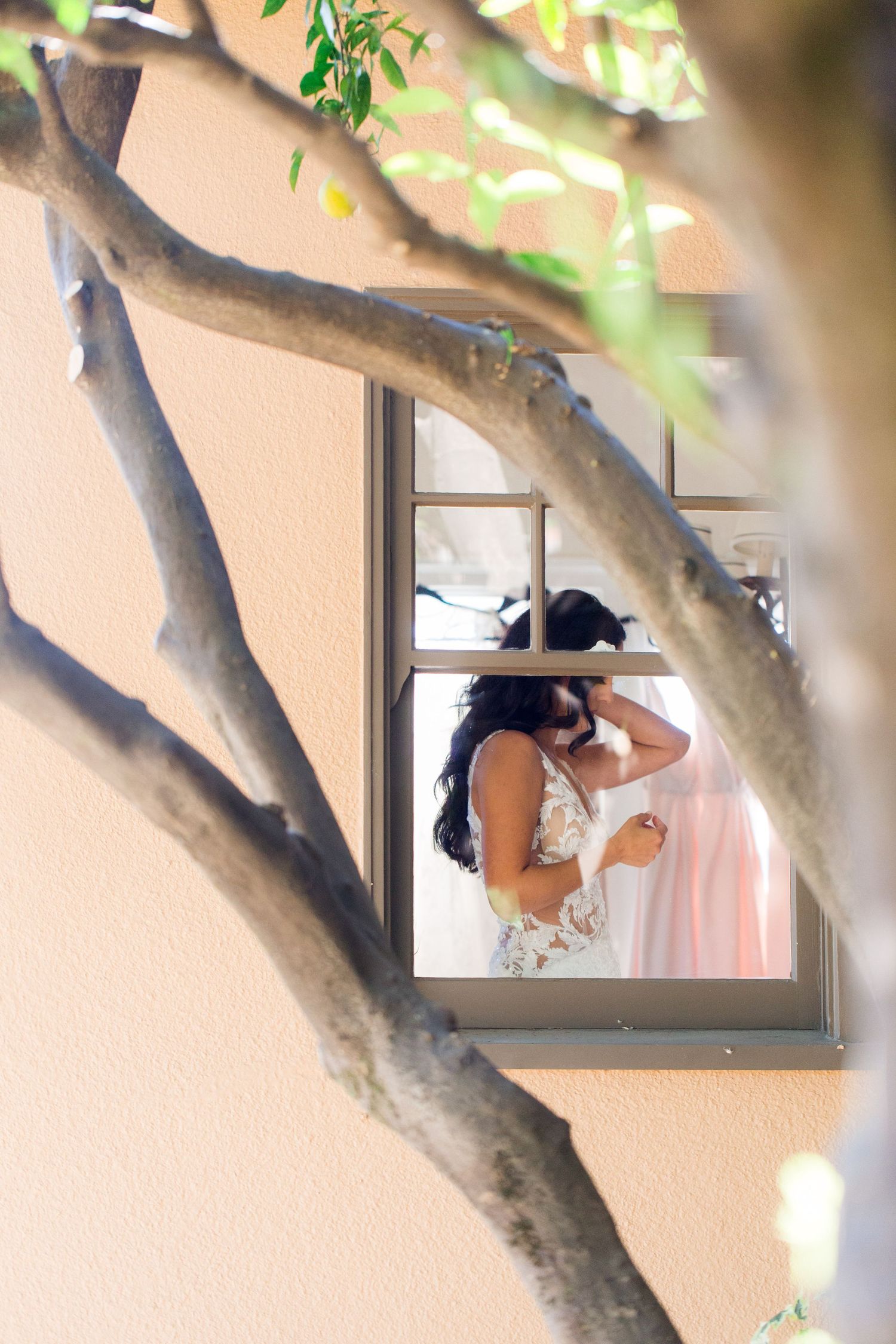 Through tree branches, a wedding preparation scene is captured in a window frame.