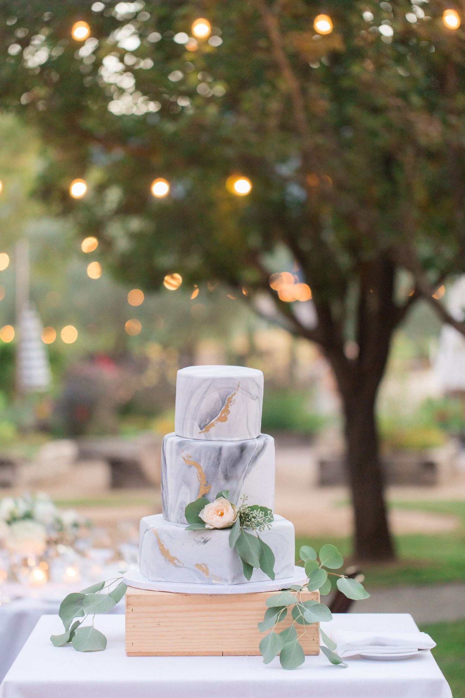 Three-tier marble-effect wedding cake decorated with fresh flowers and greenery.
