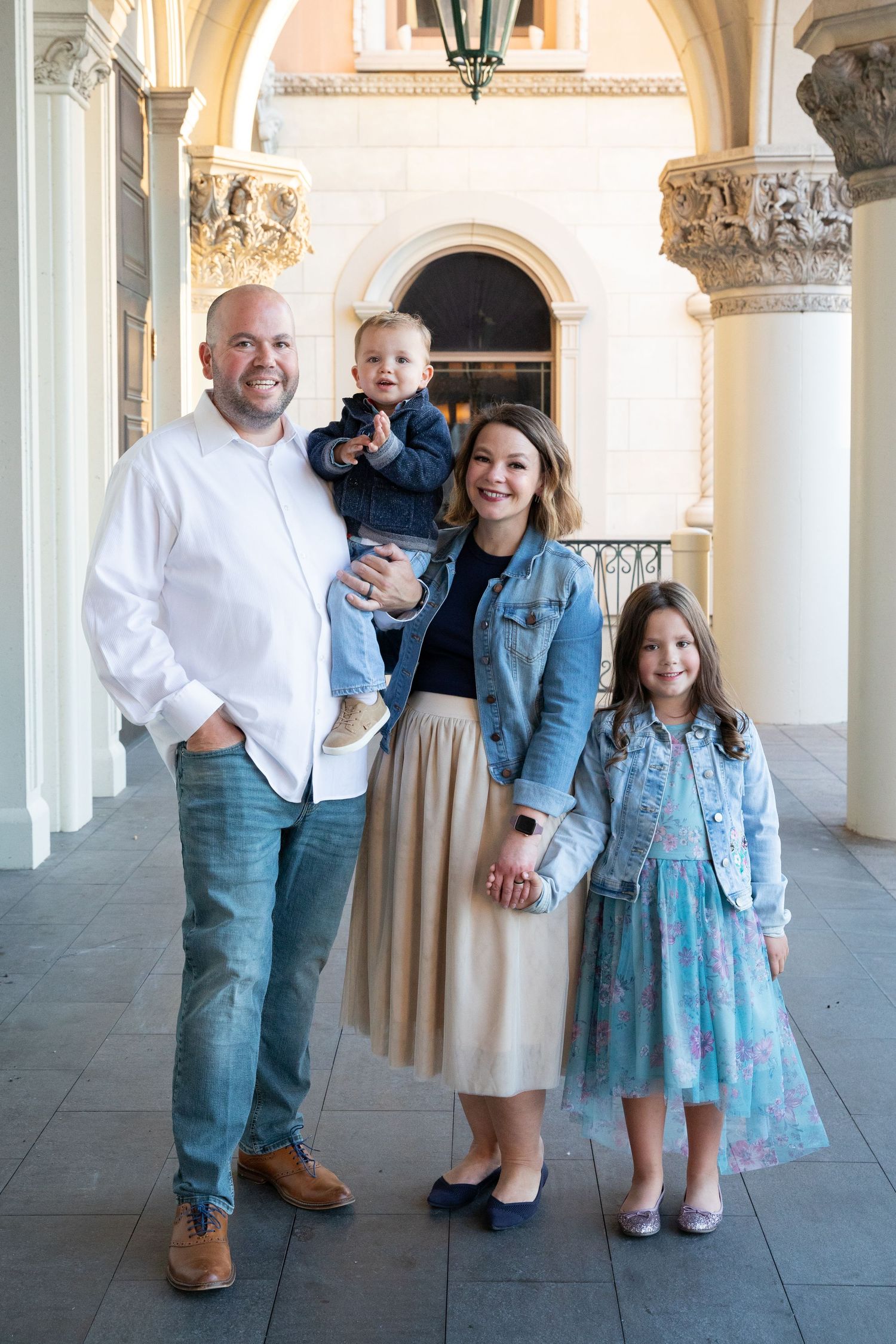 Family of four poses under ornate archway wearing coordinated denim and blue outfits.