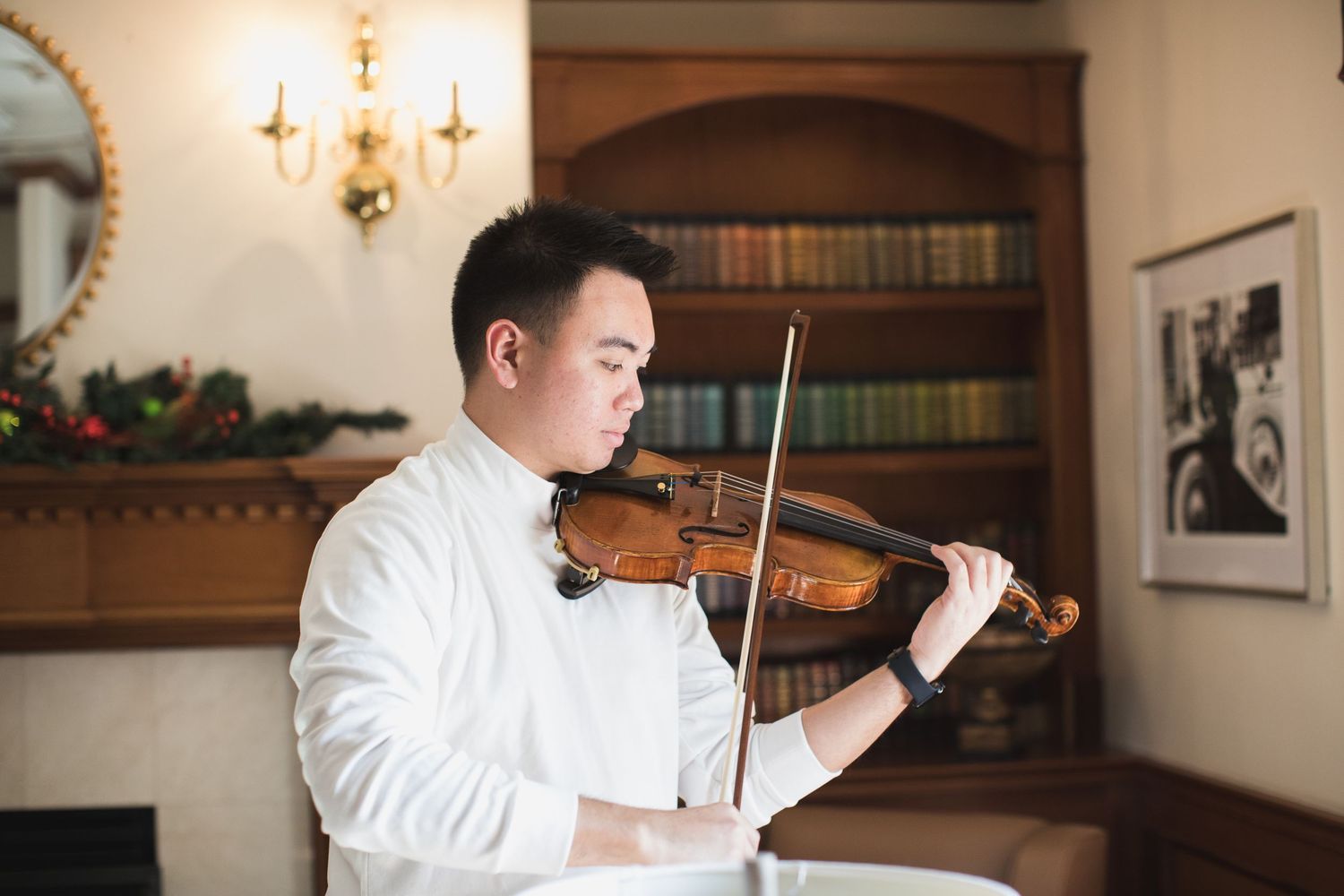Violinist in white shirt performs in elegant room with chandelier.