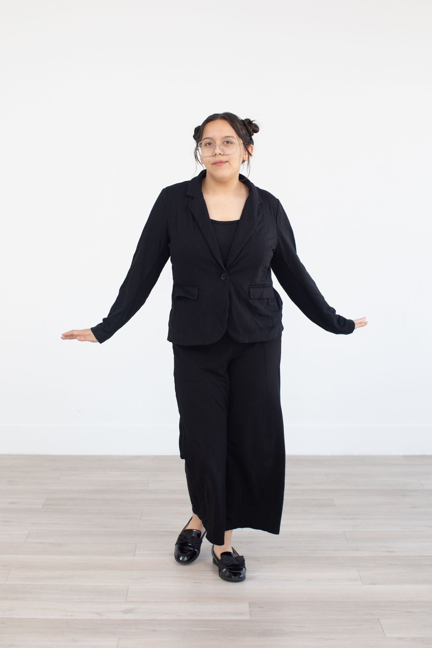 Performer in black blazer and wide-leg pants poses with arms spread.