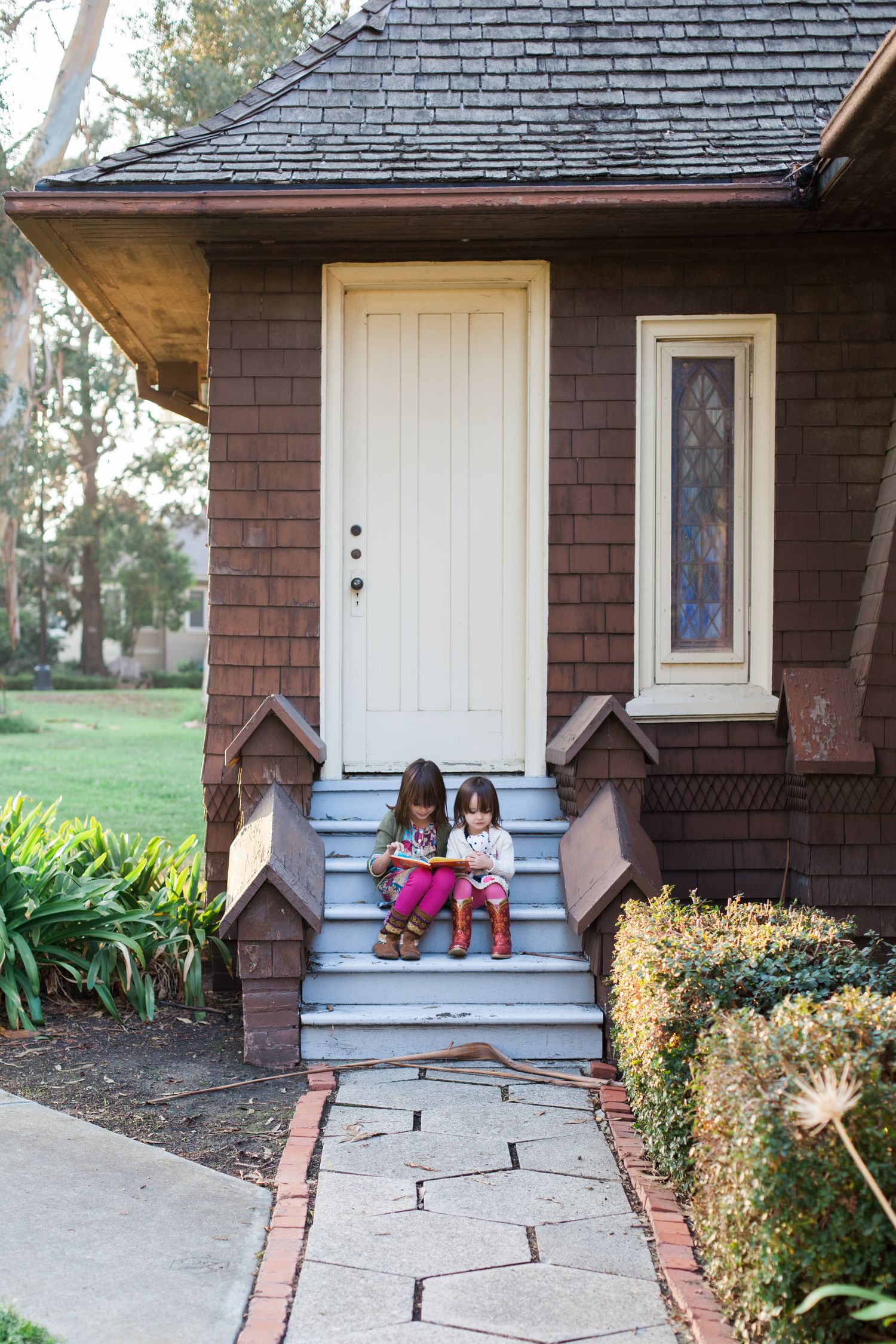 Small children sitting on front porch steps of brown craftsman style house.