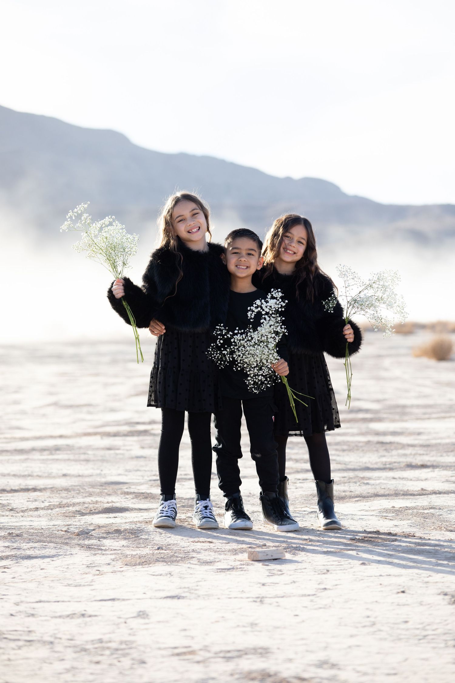 Family wearing matching black outfits posing together on a desert landscape with mountains.