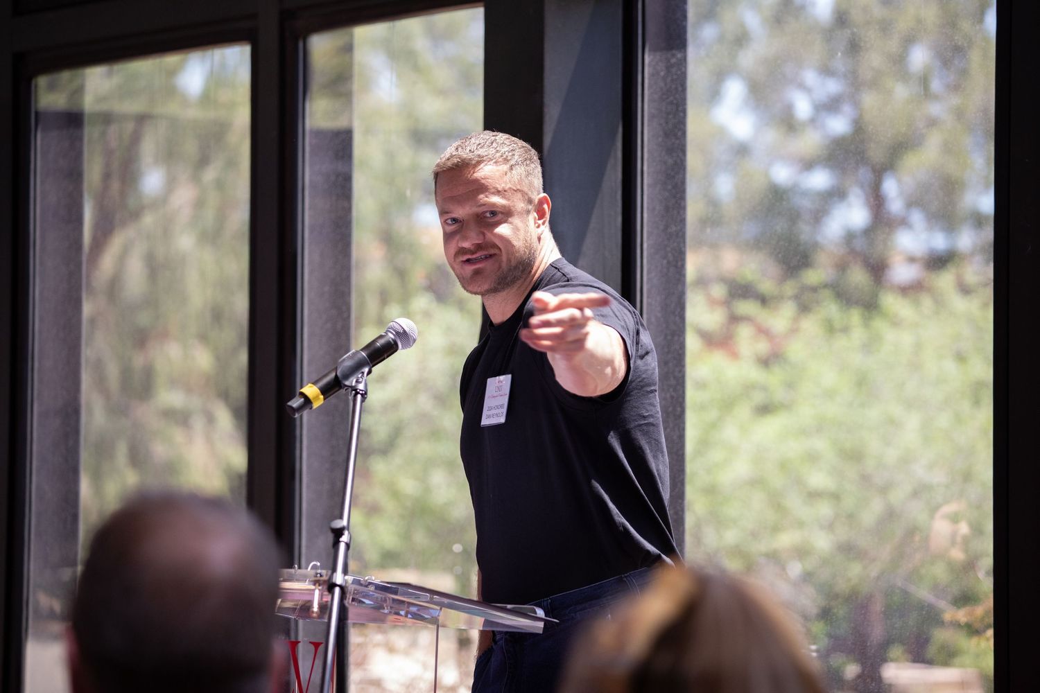 Speaker gestures while delivering remarks at podium during indoor event.