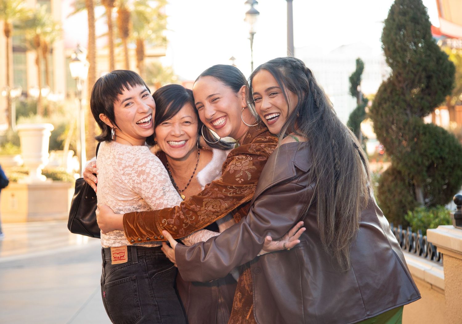 Group of friends laughing and hugging outdoors in stylish winter outfits.
