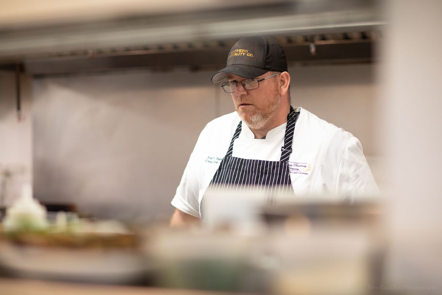 Chef in striped apron and baseball cap working in a professional kitchen.