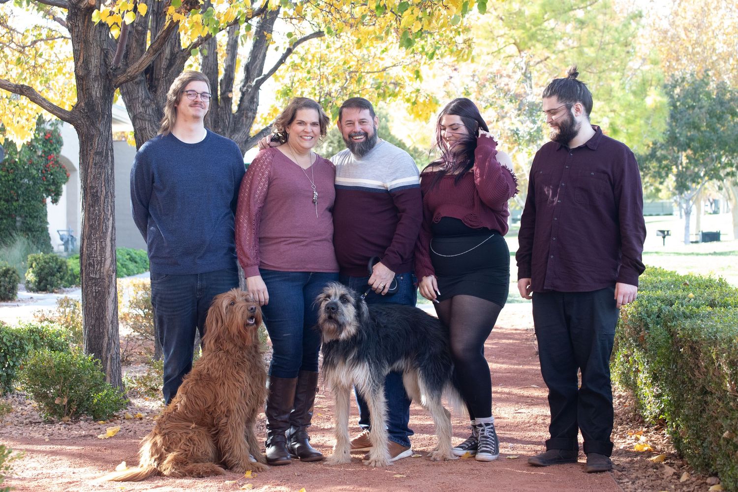 Family with two dogs poses together on a brick path surrounded by autumn trees.