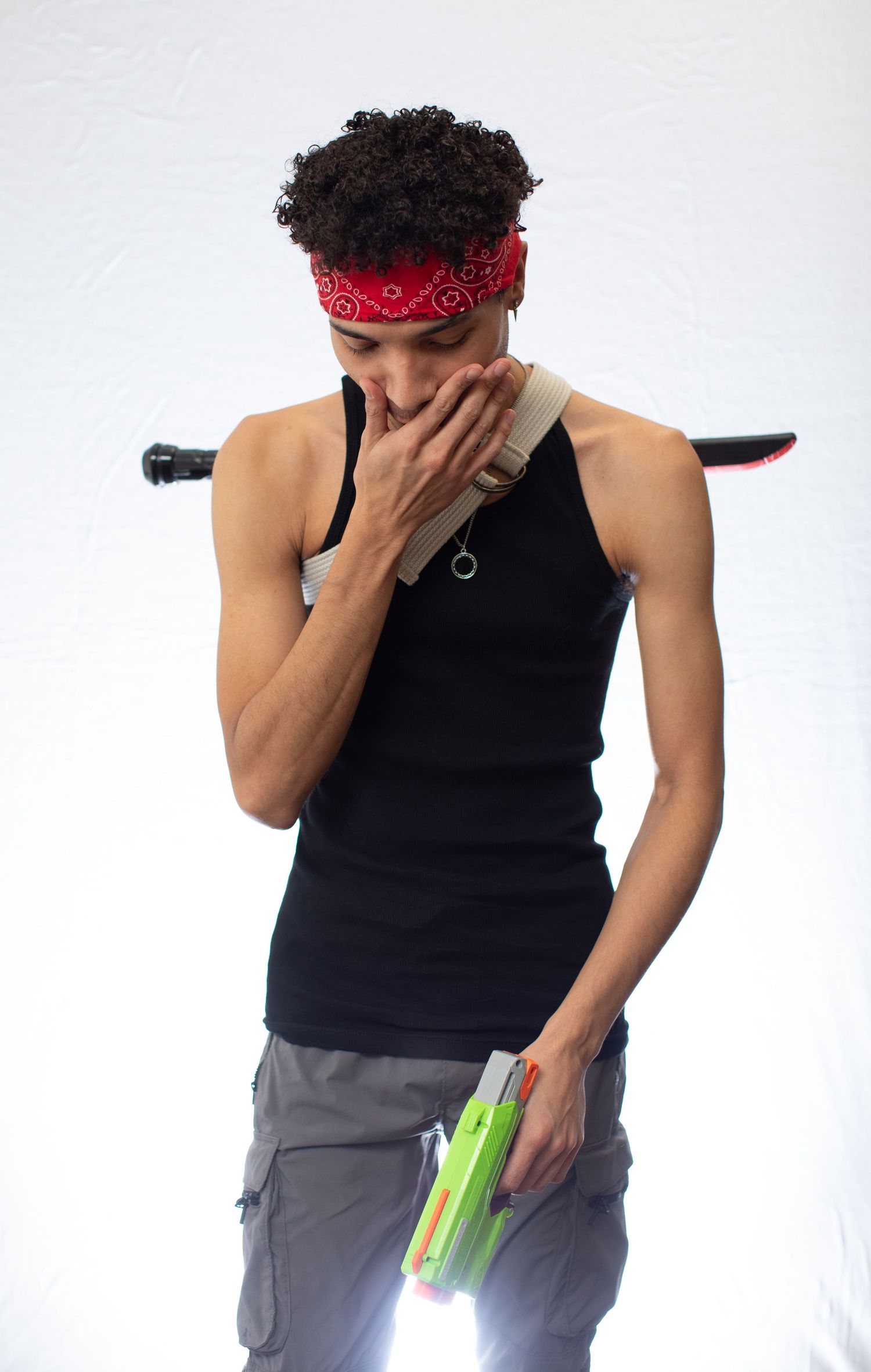 Athletic person in black tank top and red bandana covering mouth while holding celery sticks.