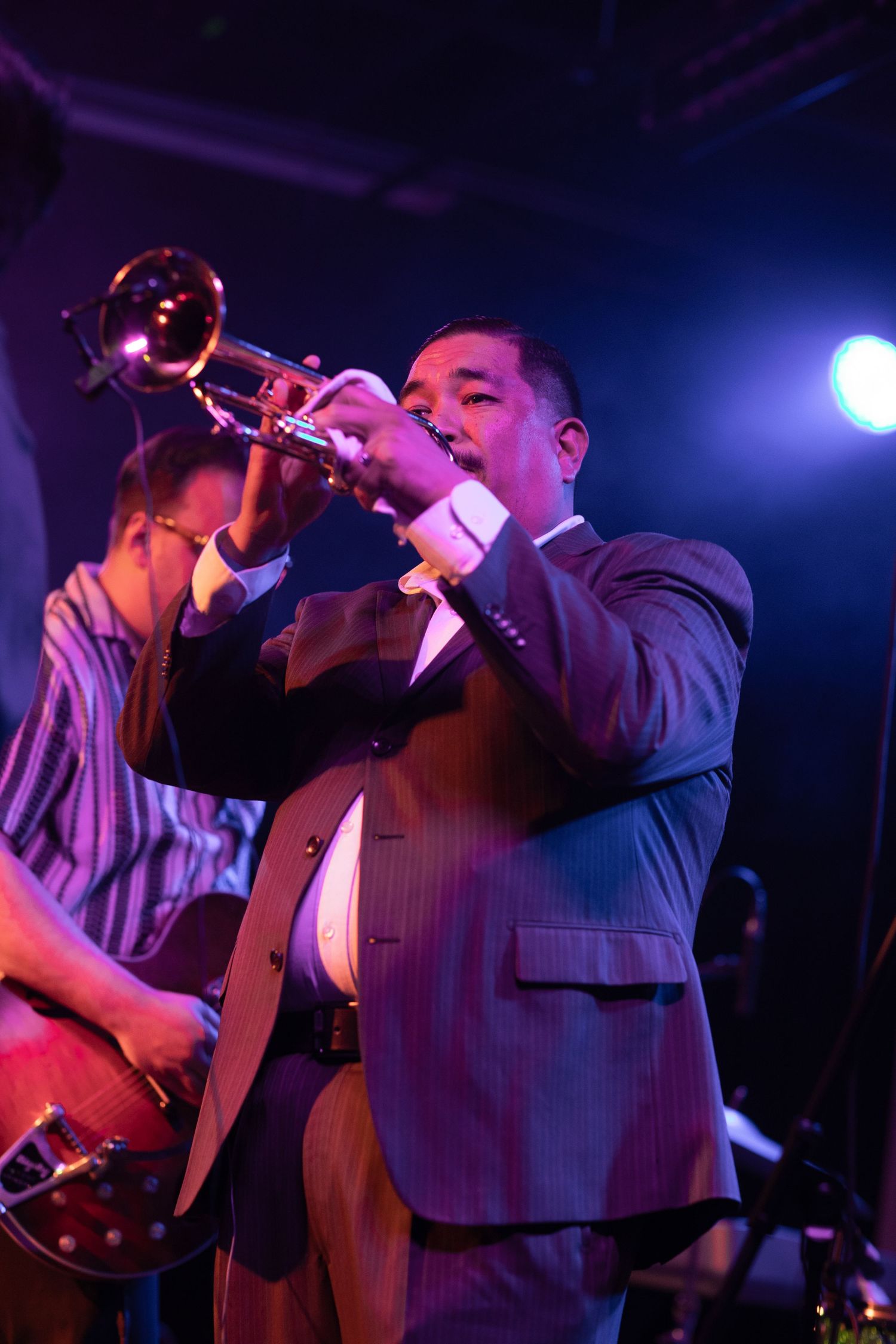 Trumpet player in suit performs jazz music under blue stage spotlights.