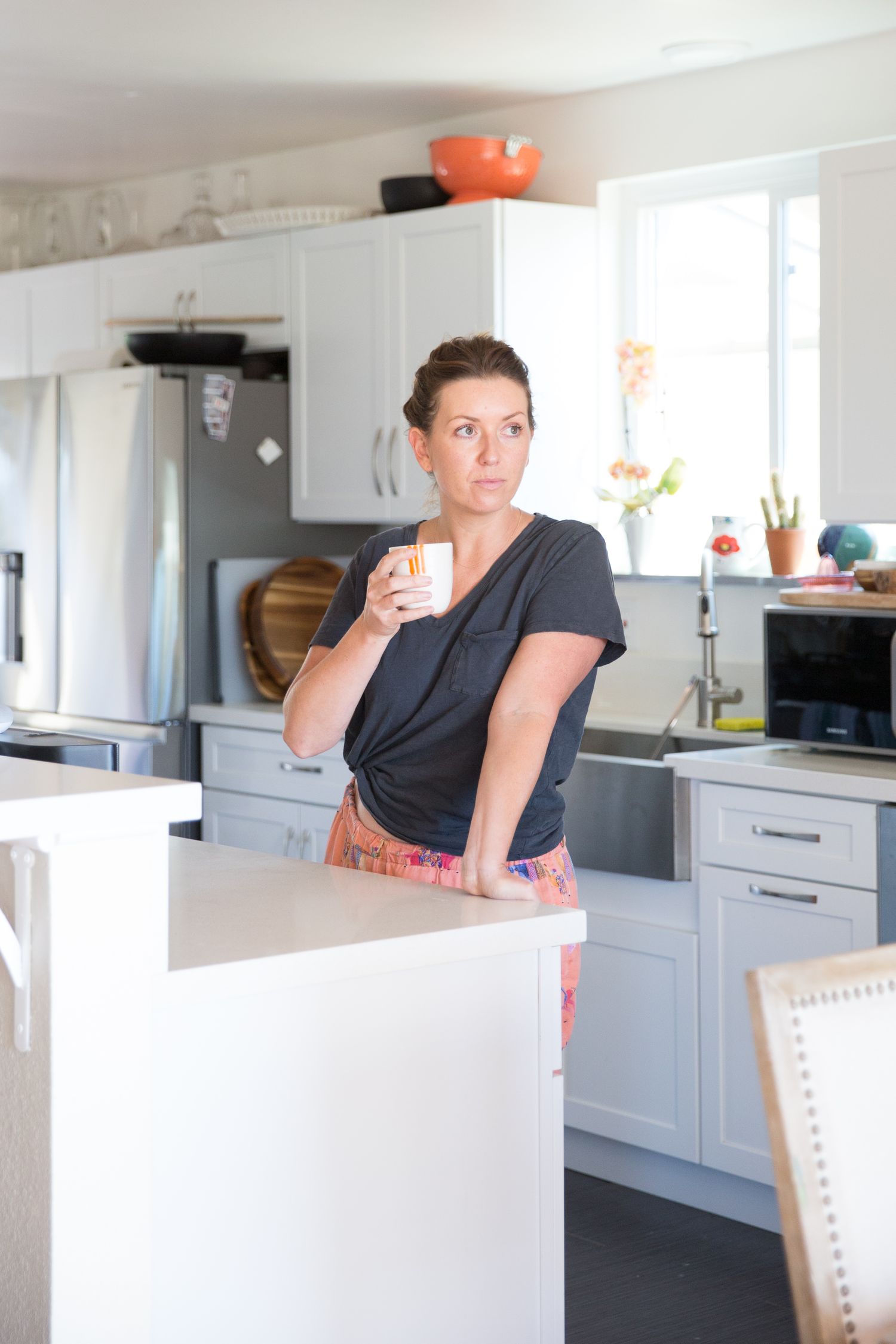 Woman in black shirt holding coffee mug in modern kitchen with white cabinets.