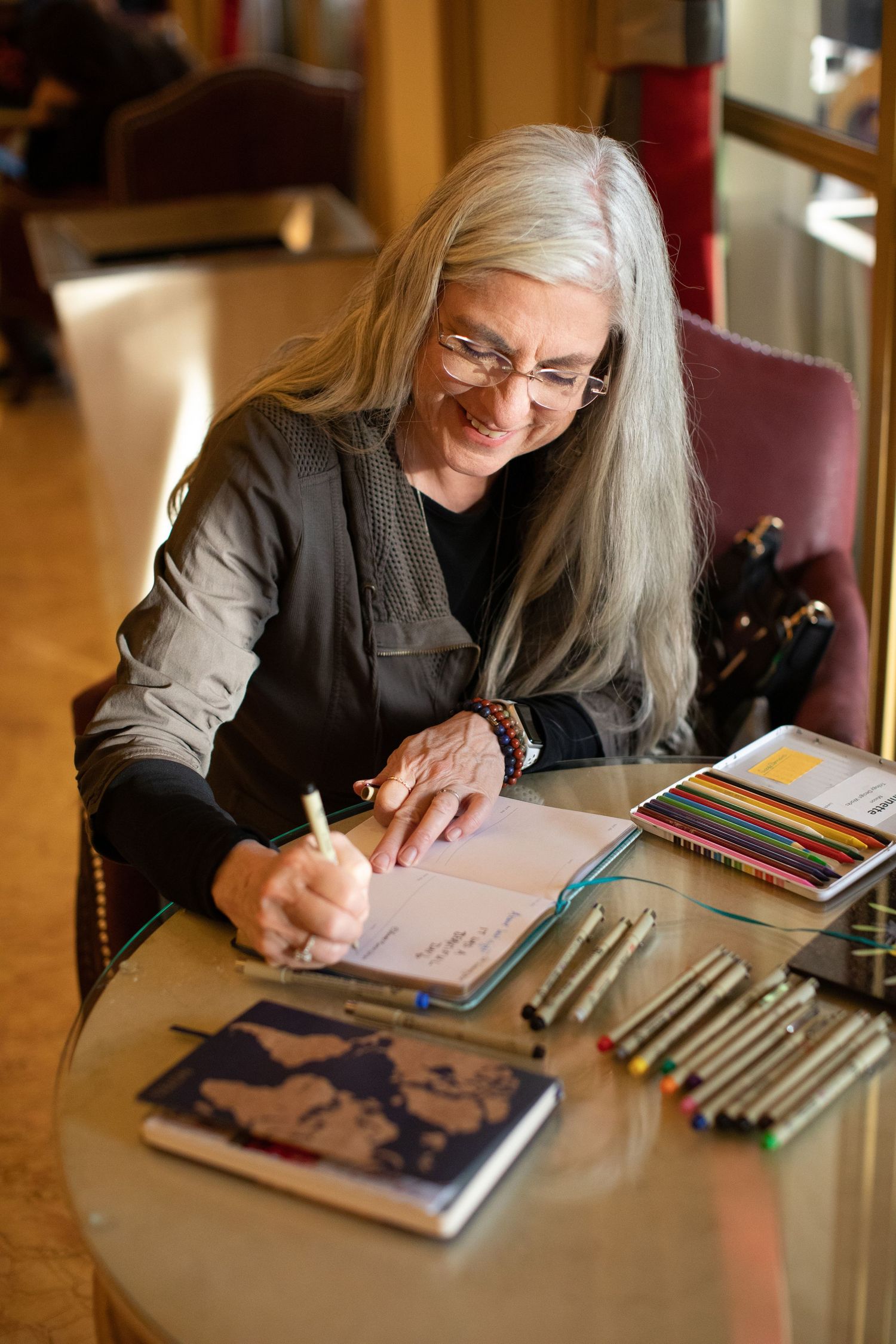 Artist working on drawings with colorful pens and materials at a wooden desk.