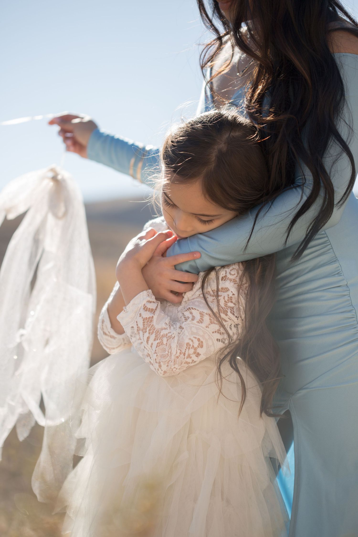 A delicate white lace dress hangs in soft natural light against a bright background.