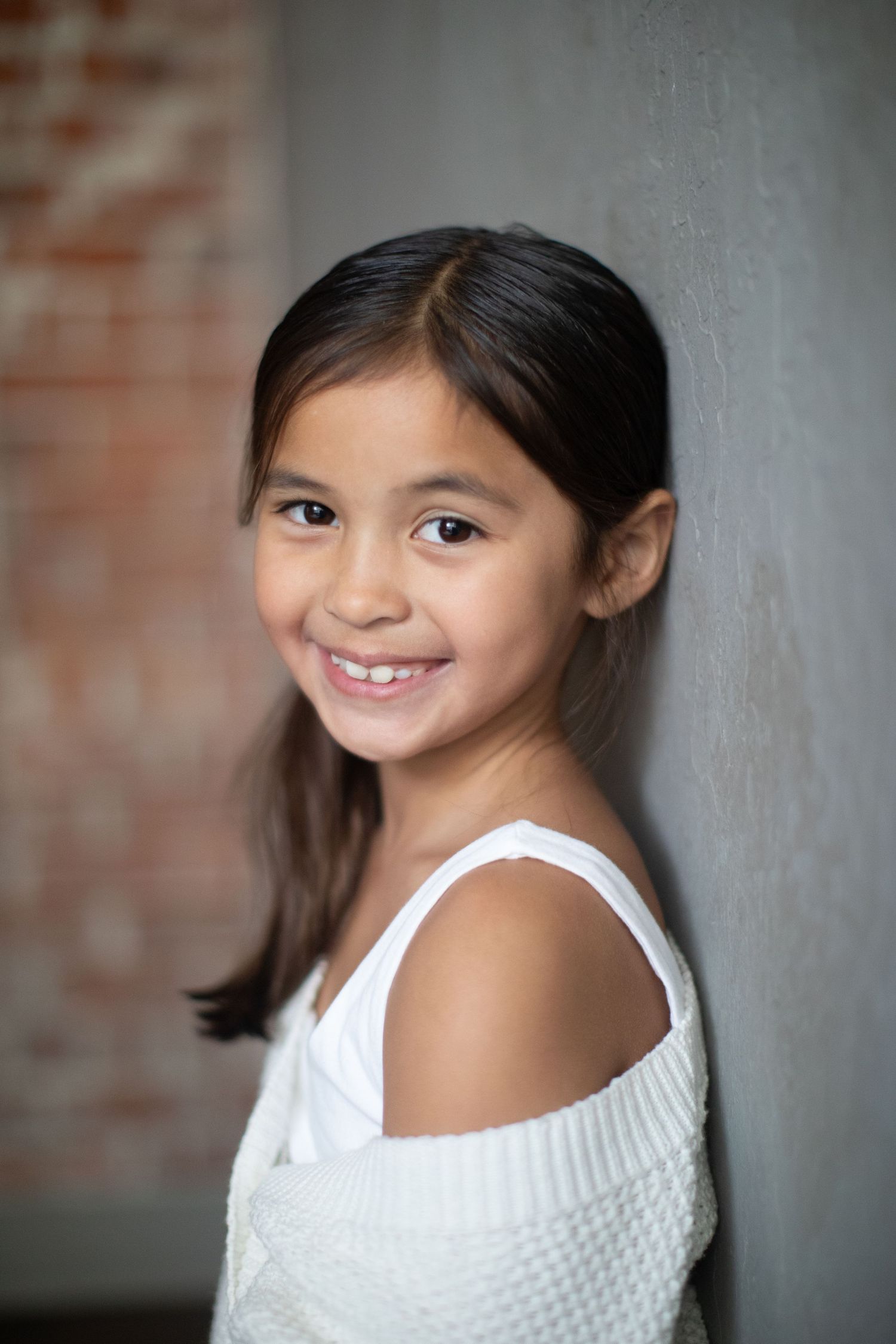 Portrait of young person in white top smiling against grey wall background.