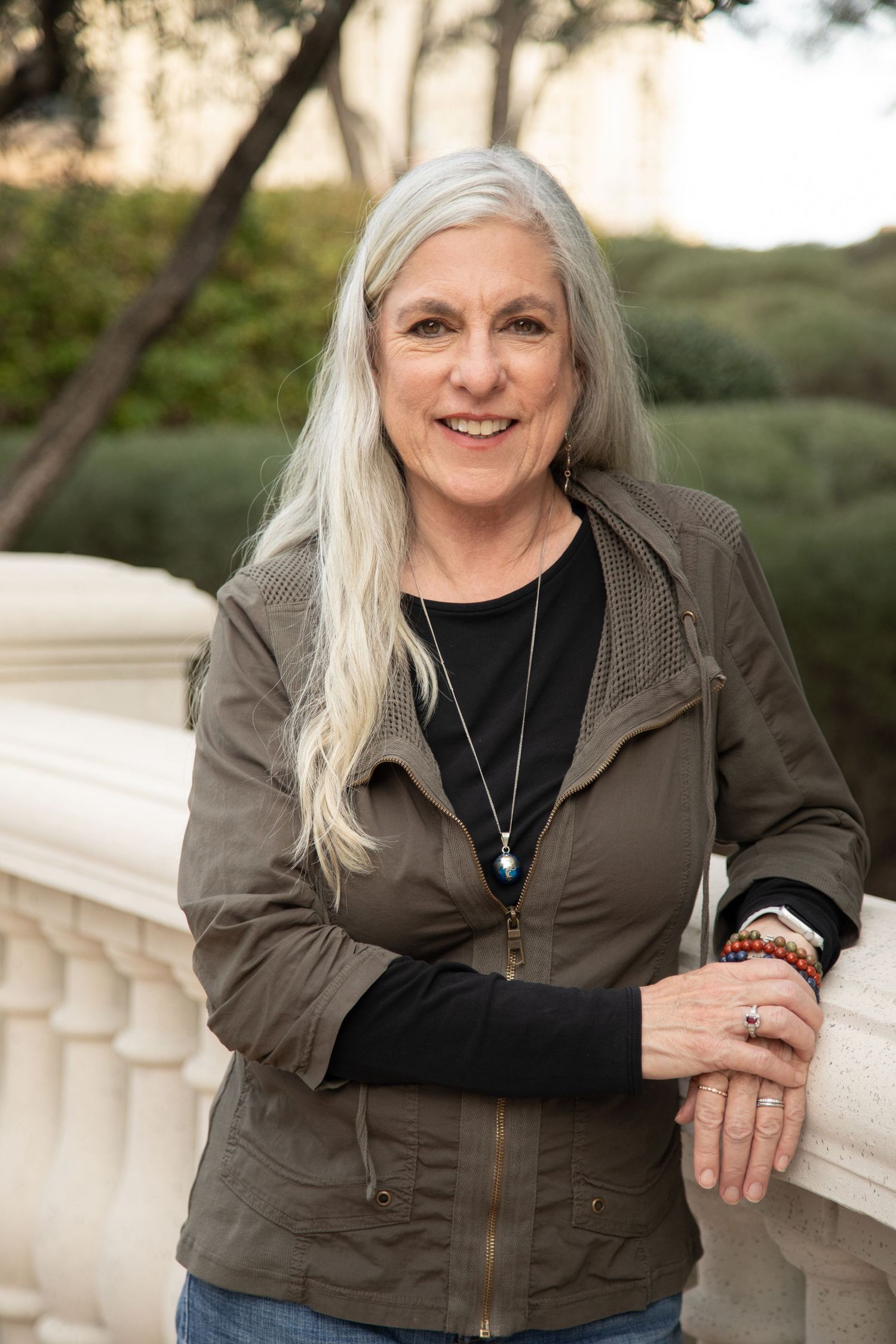 A woman with long silver hair wearing a casual jacket poses outdoors.