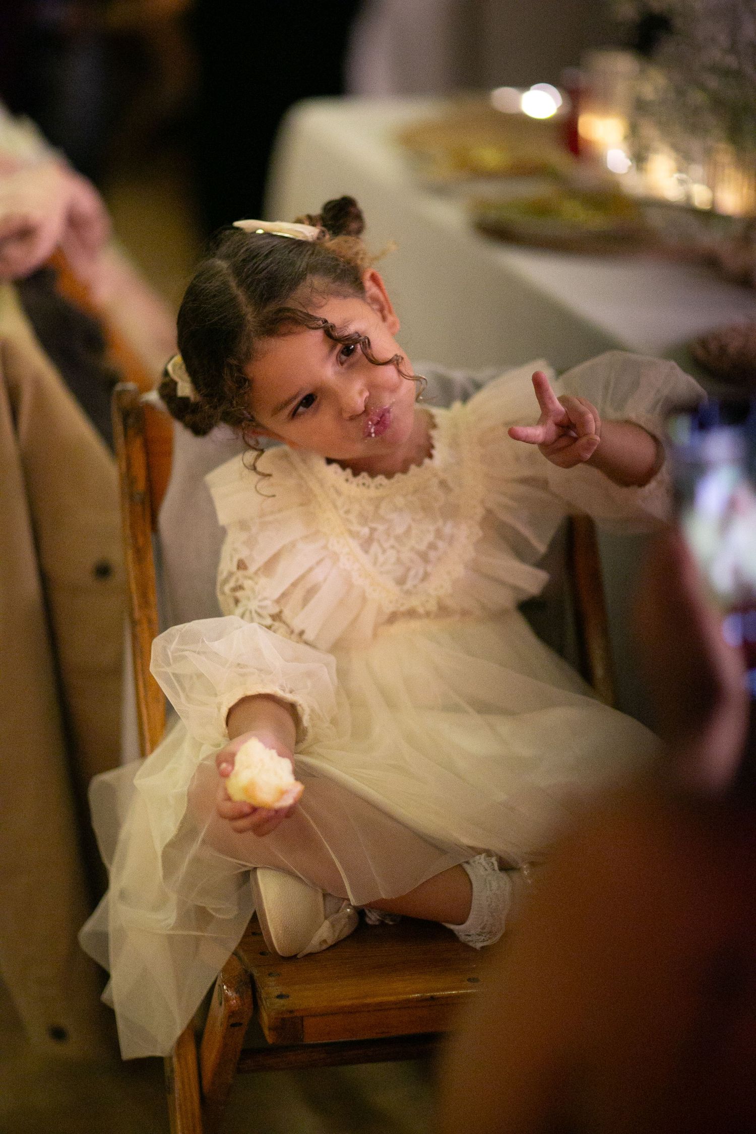 Young girl in a frilly white dress making playful expressions during a celebration.