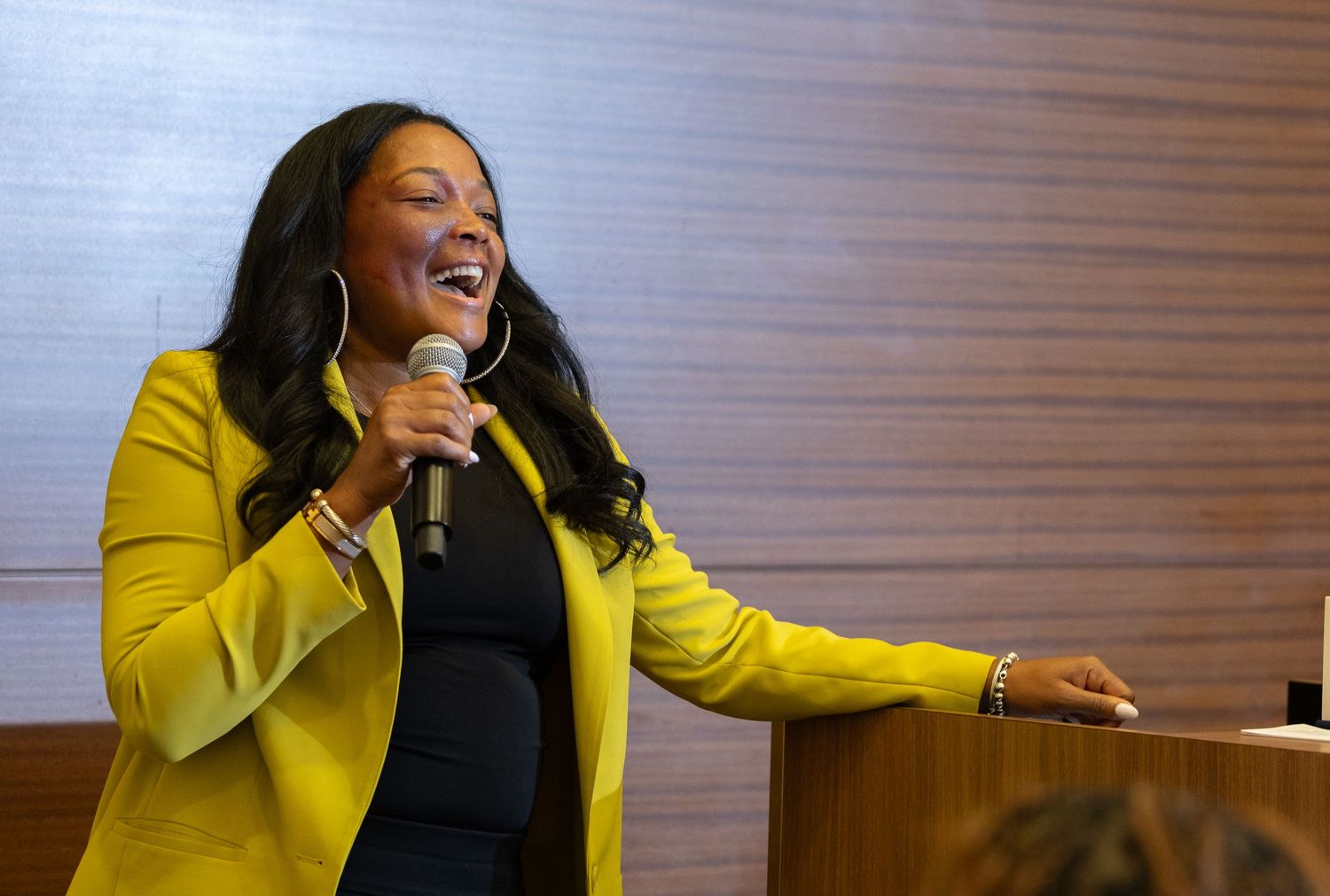 Professional speaker in yellow blazer addressing audience at corporate event.