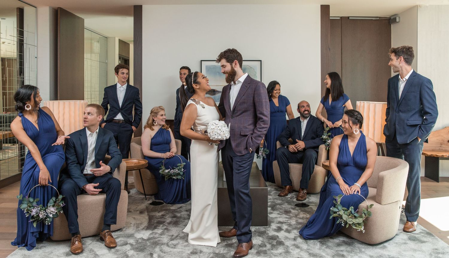 Wedding party gathered in an elegant hotel lobby with bridesmaids in navy dresses and groomsmen in dark suits.