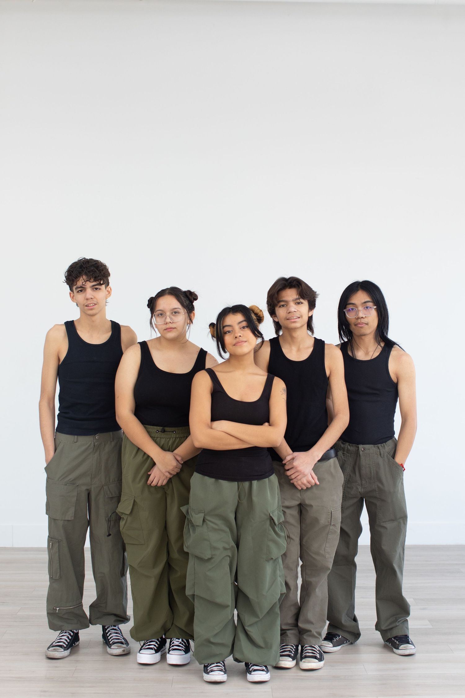 Band members in black tank tops and cargo pants pose together against white background.