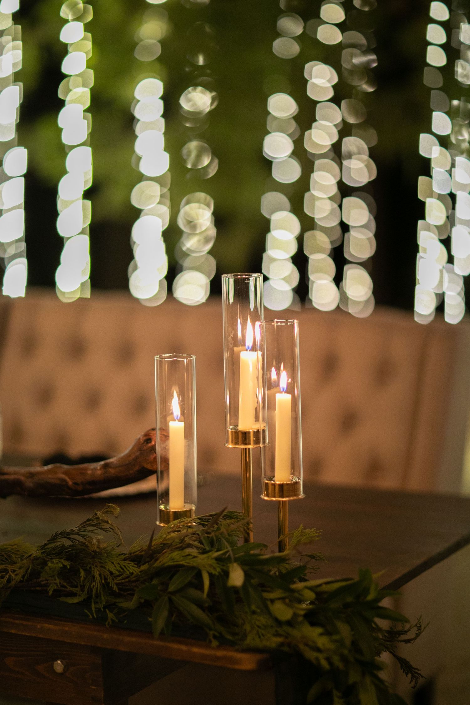 Glass candle holders with lit candles against a bokeh light background and greenery decoration.
