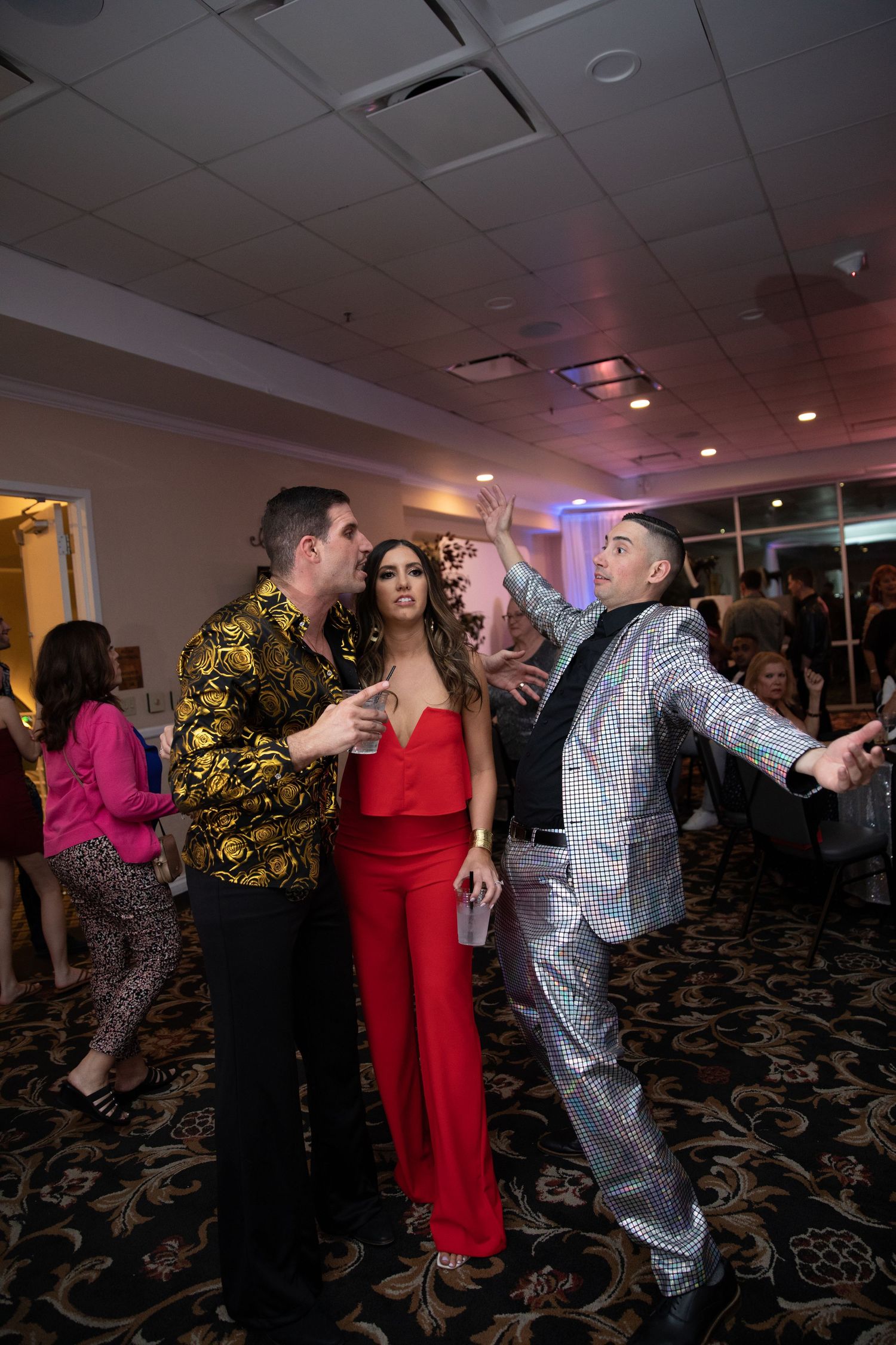 Guests dance in formal attire at an indoor reception with red and purple ambient lighting.