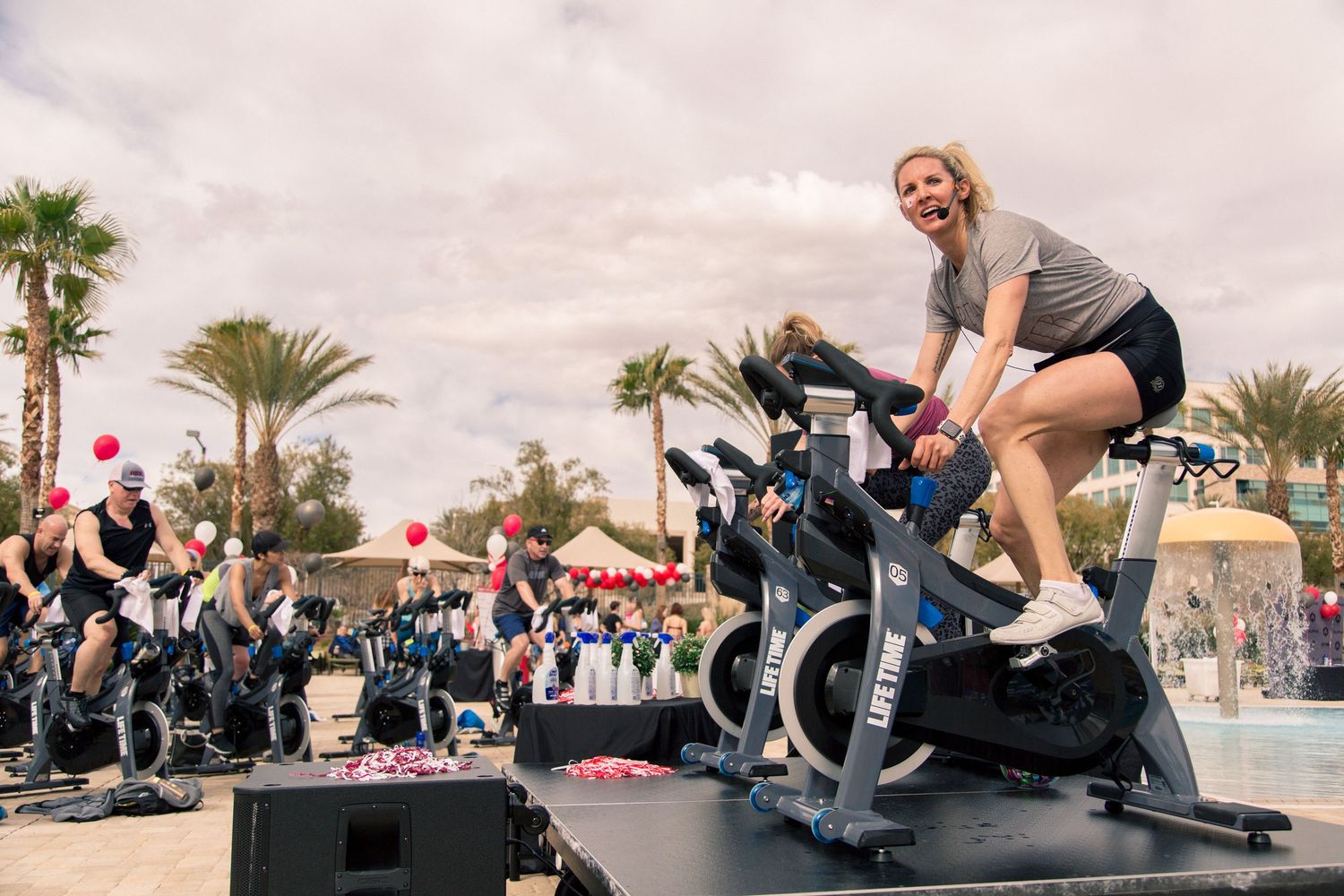 People exercising on spin bikes during an outdoor fitness class with palm trees in background.