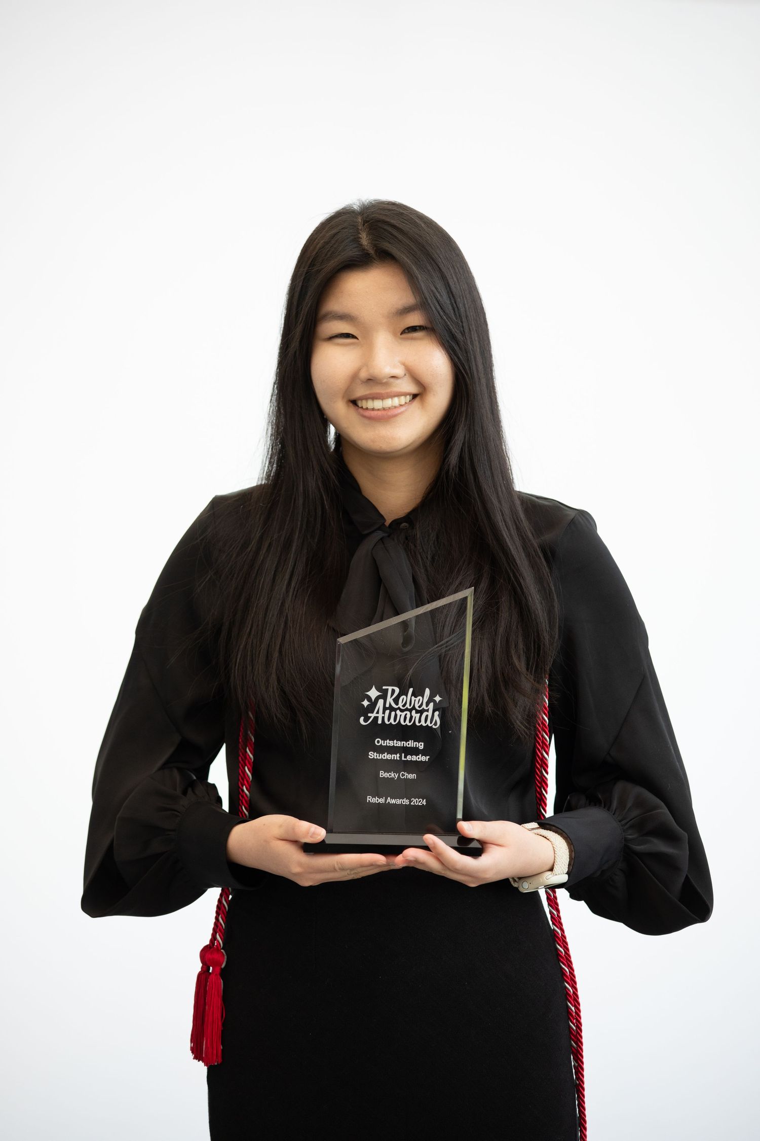Graduate in black academic regalia holding diploma case against white background.