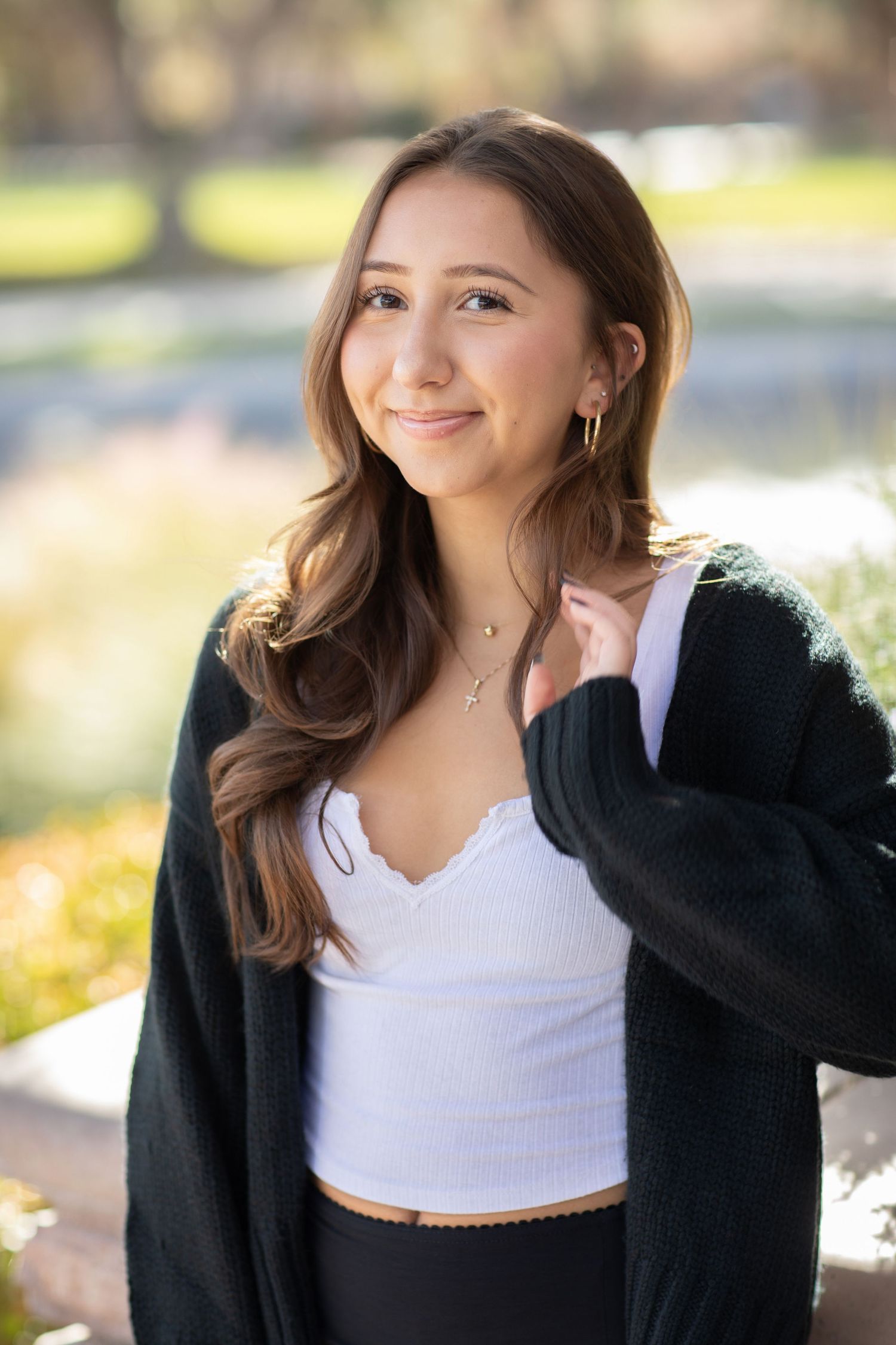 Portrait of young woman in black cardigan and white top smiling outdoors on sunny day.