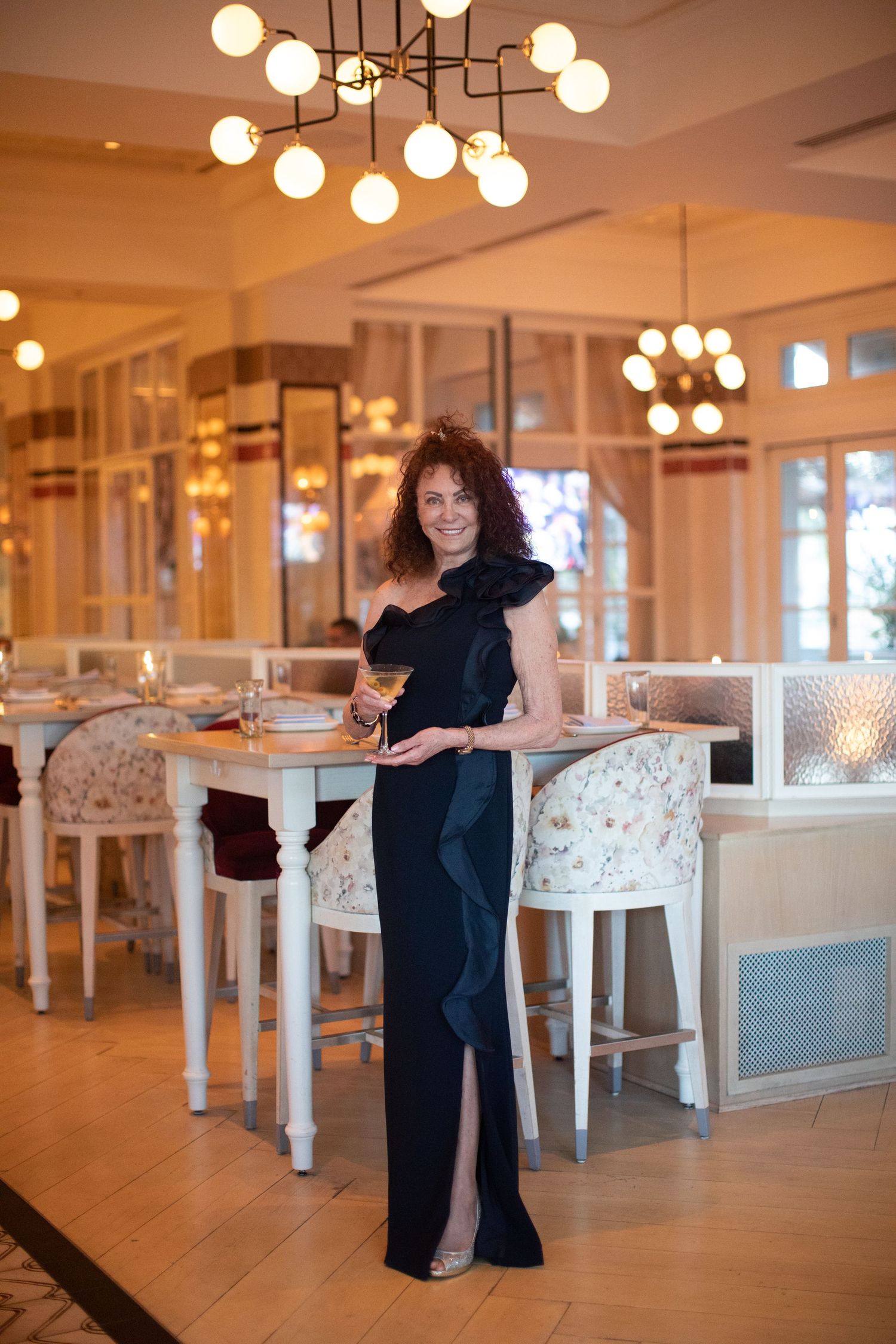 Person posing in formal black dress at upscale restaurant with spherical light fixtures.