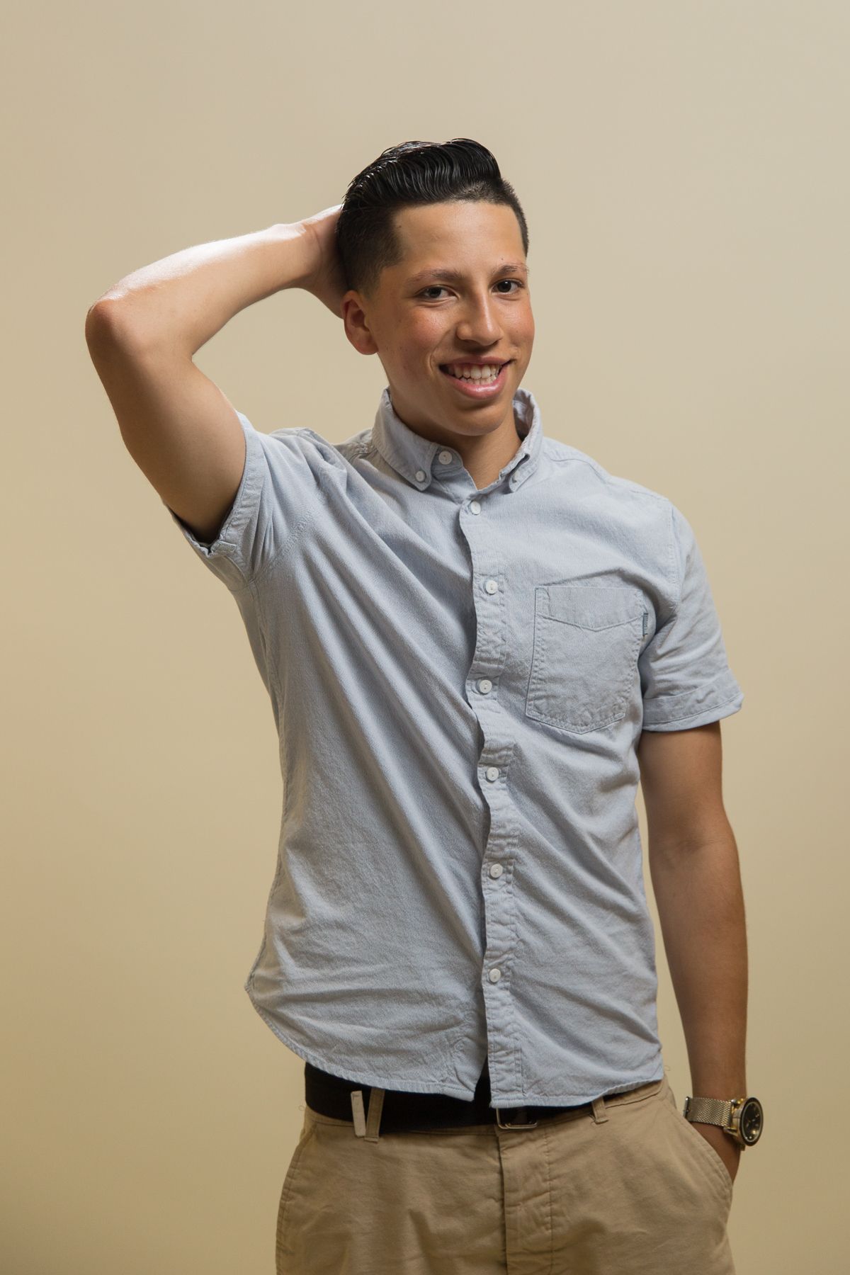 Portrait against beige wall shows person in gray button-down shirt.