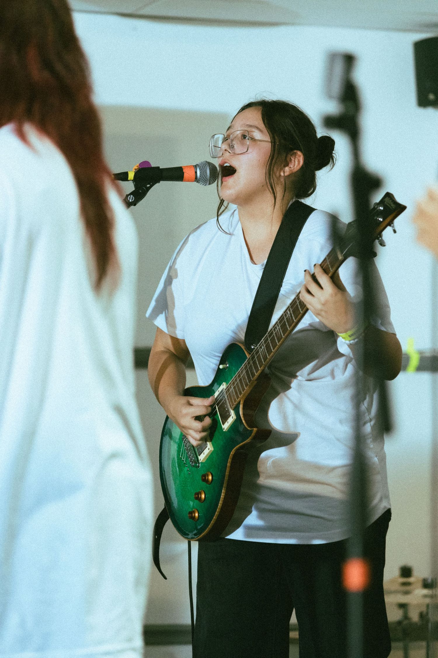 Performer playing green electric guitar while singing in a bright studio setting.