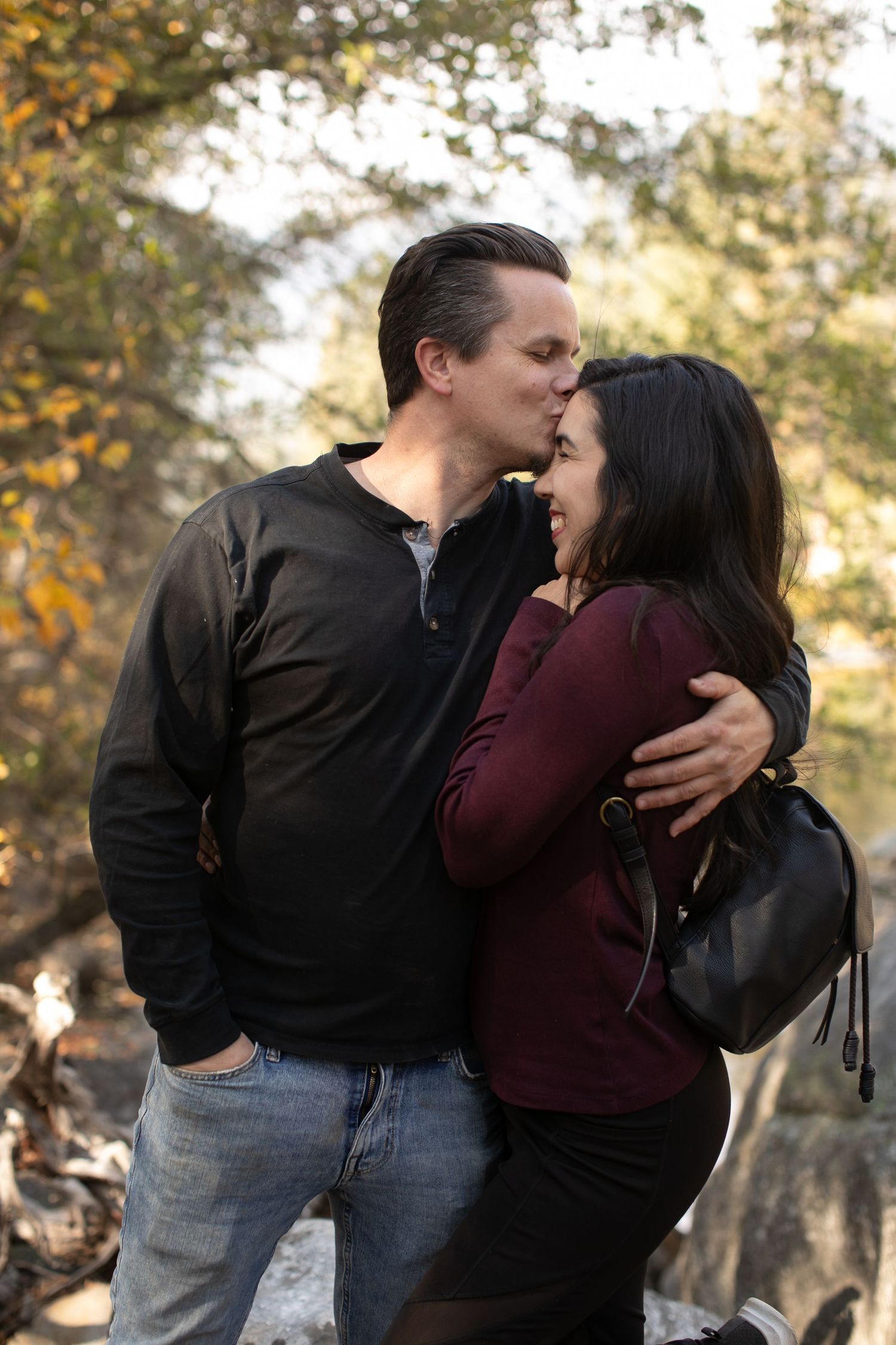 A romantic couples photo session shows tender moments between partners wearing burgundy and black against an autumn backdrop.