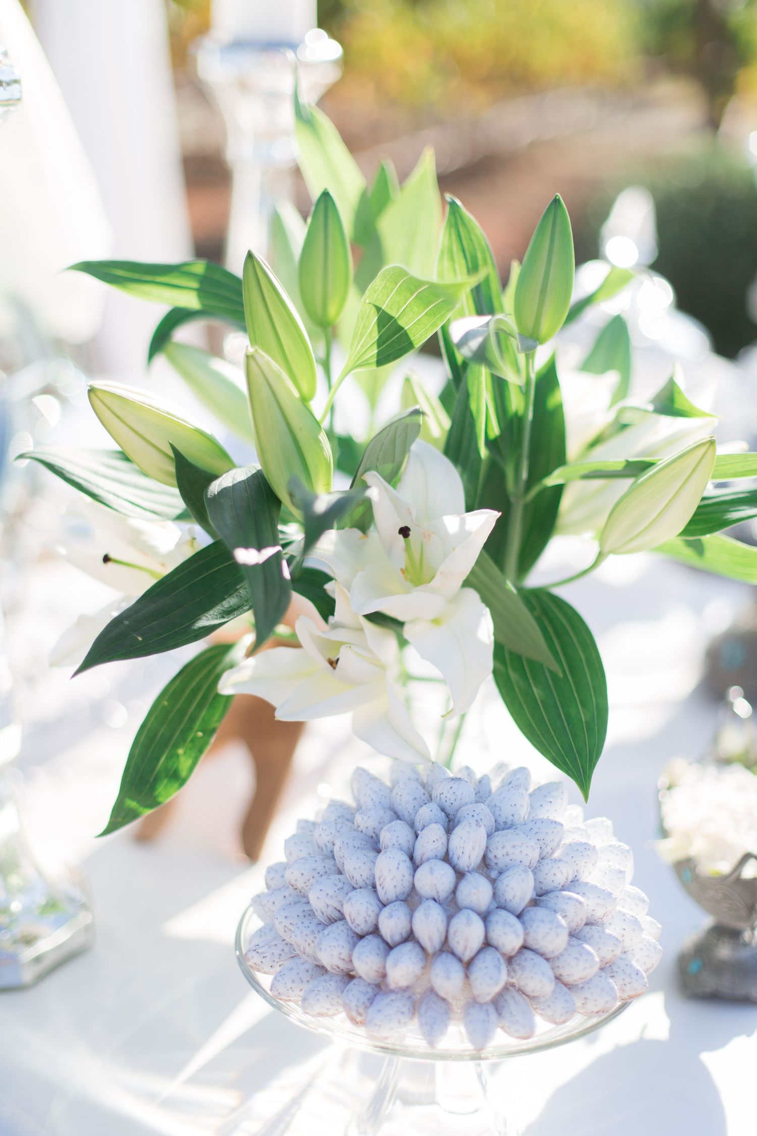 White lily floral centerpiece with blue candy arrangement on an elegant table setting.
