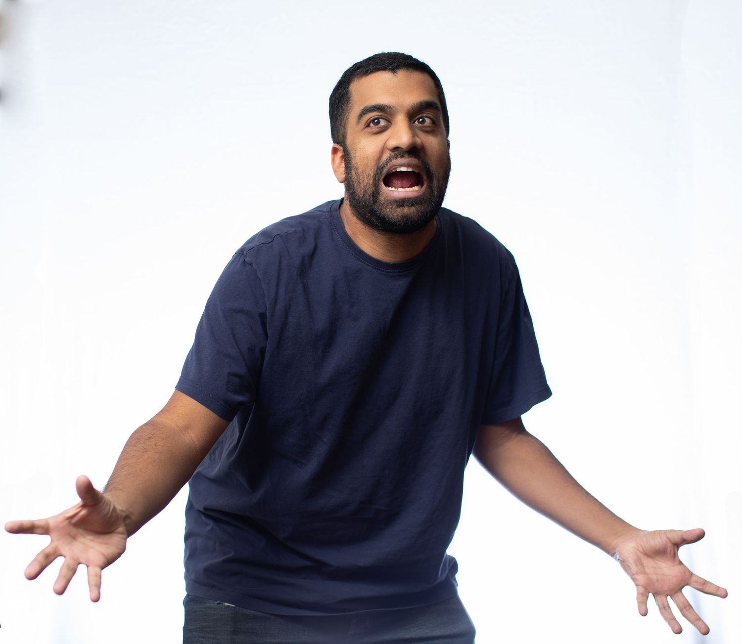 Person in navy t-shirt expressing exasperation with outstretched arms against white background.
