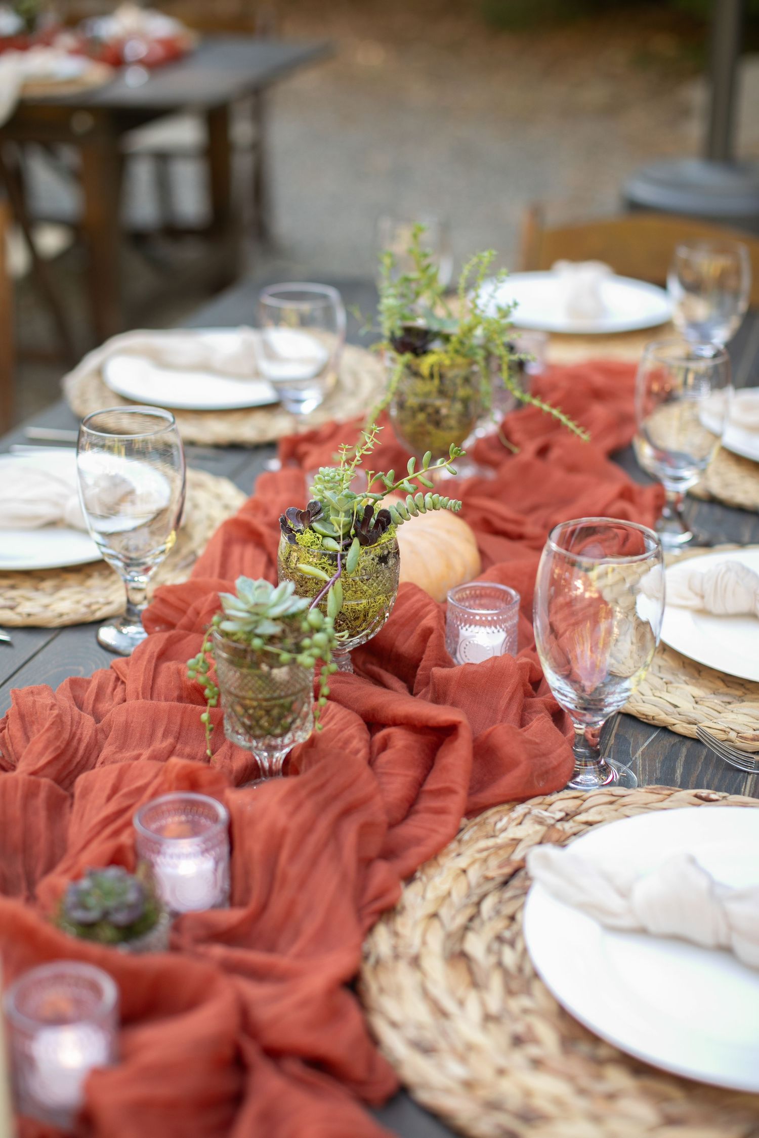 Elegant table setting with terracotta runner and greenery centerpieces for outdoor dining.