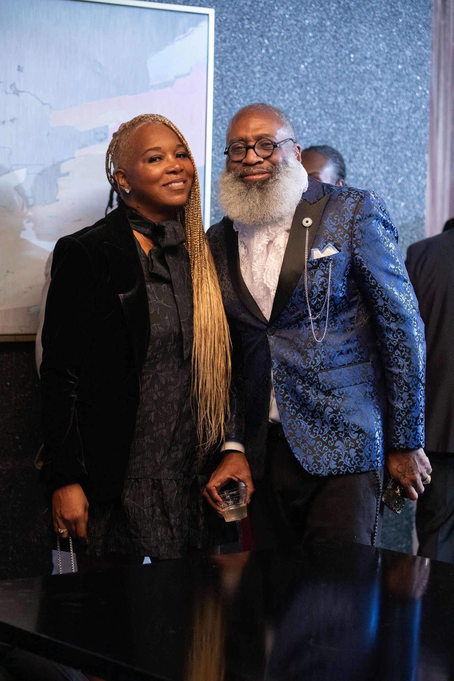 Two guests pose together at an event, one wearing a black dress and one in a patterned blue blazer.