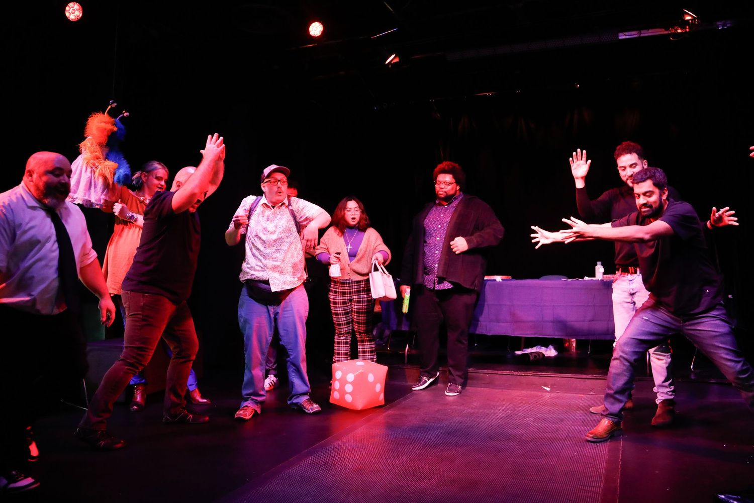 Theatrical performance with multiple actors moving across a purple-lit stage.