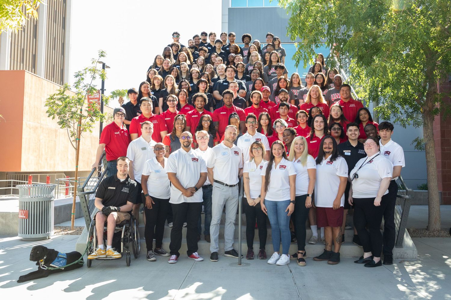 A formal group photo of students and staff in coordinated outfits standing outdoors.