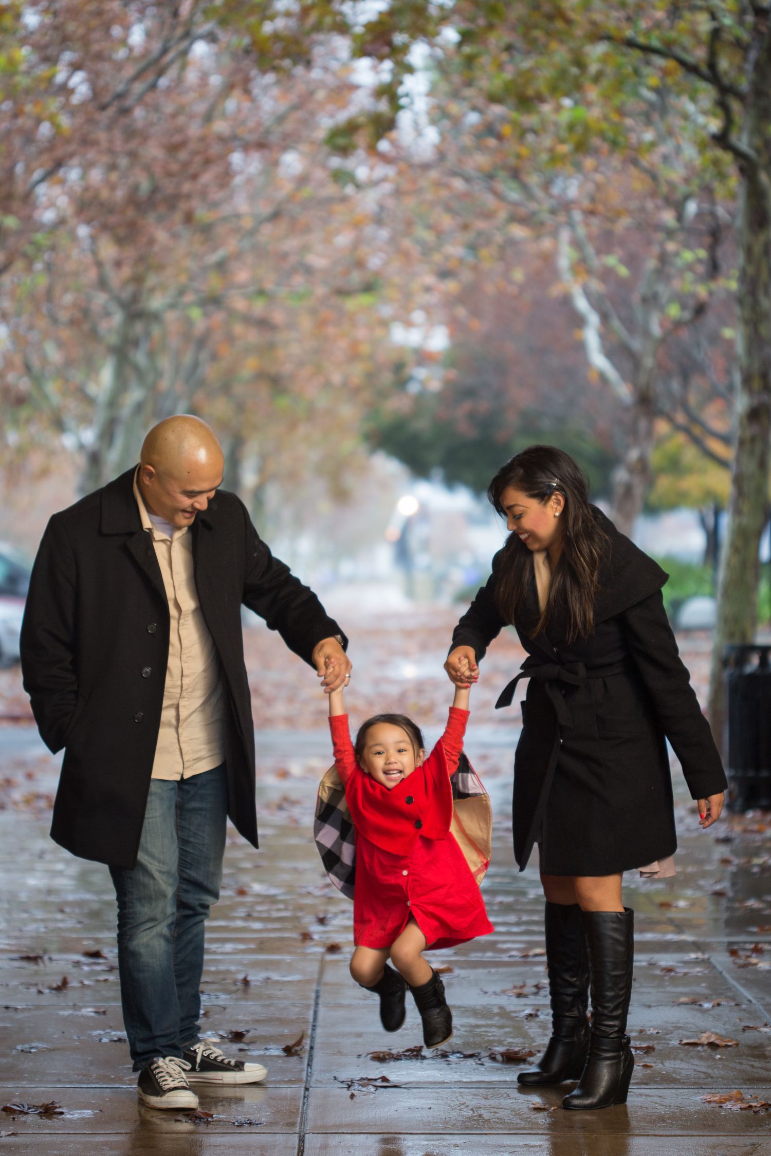 Family playing together on wet autumn sidewalk with falling leaves.