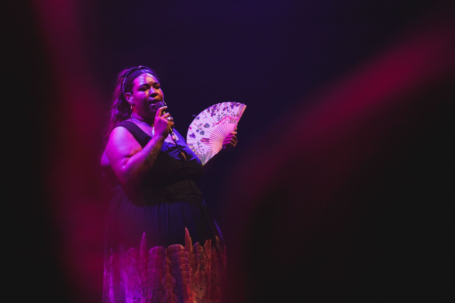 Singer performs on darkened stage illuminated by purple spotlights with a handheld prop.