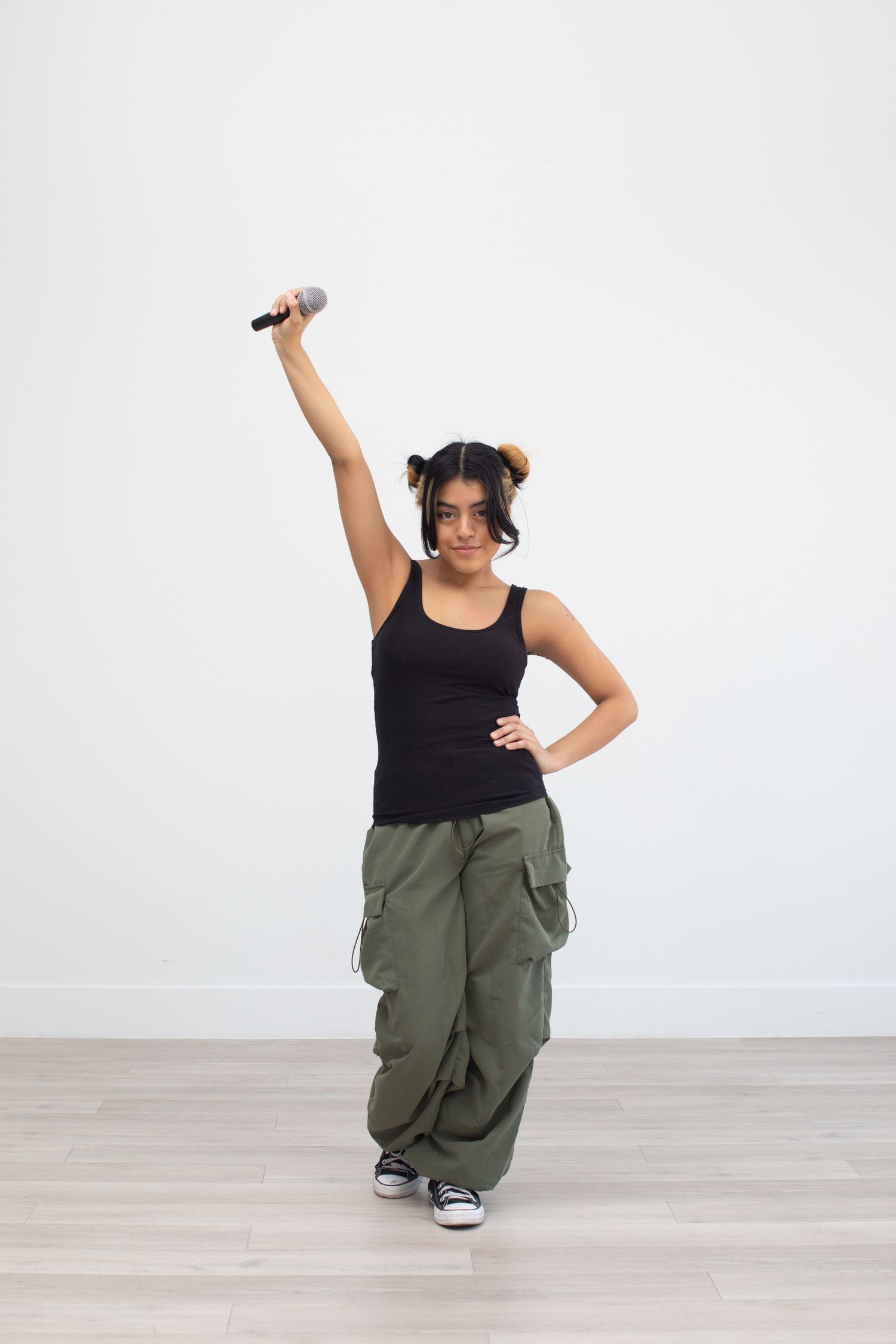 Performer in black tank top and cargo pants strikes dynamic pose while holding microphone.
