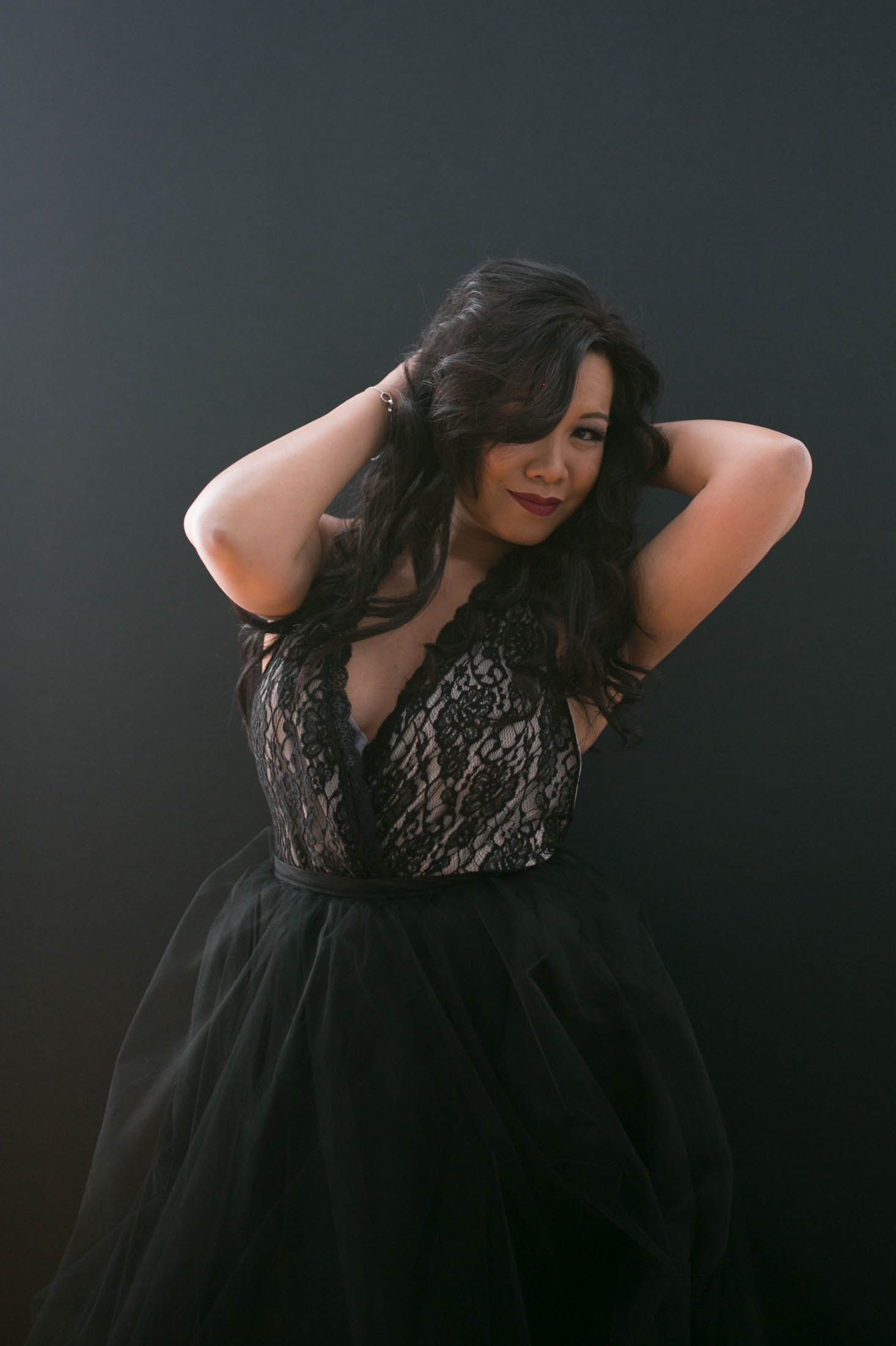 Portrait of person in elegant black lace and tulle gown against dark background.