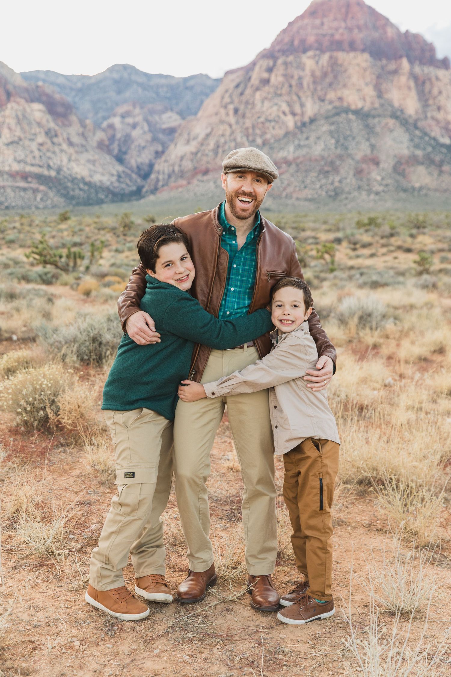 Family portrait of three people hugging and smiling against backdrop of red rock mountains.
