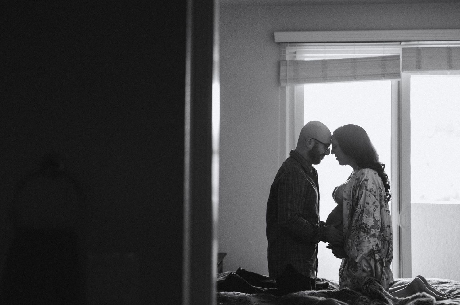 Silhouetted couple shares intimate moment near window.