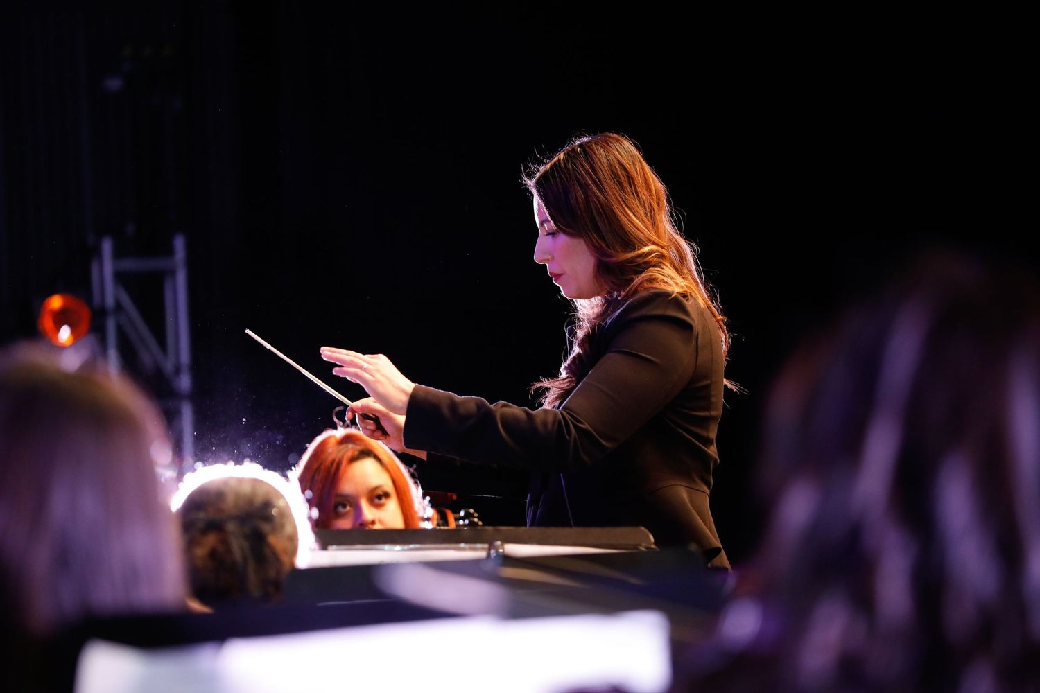 Conductor leading orchestra during performance with dramatic stage lighting.