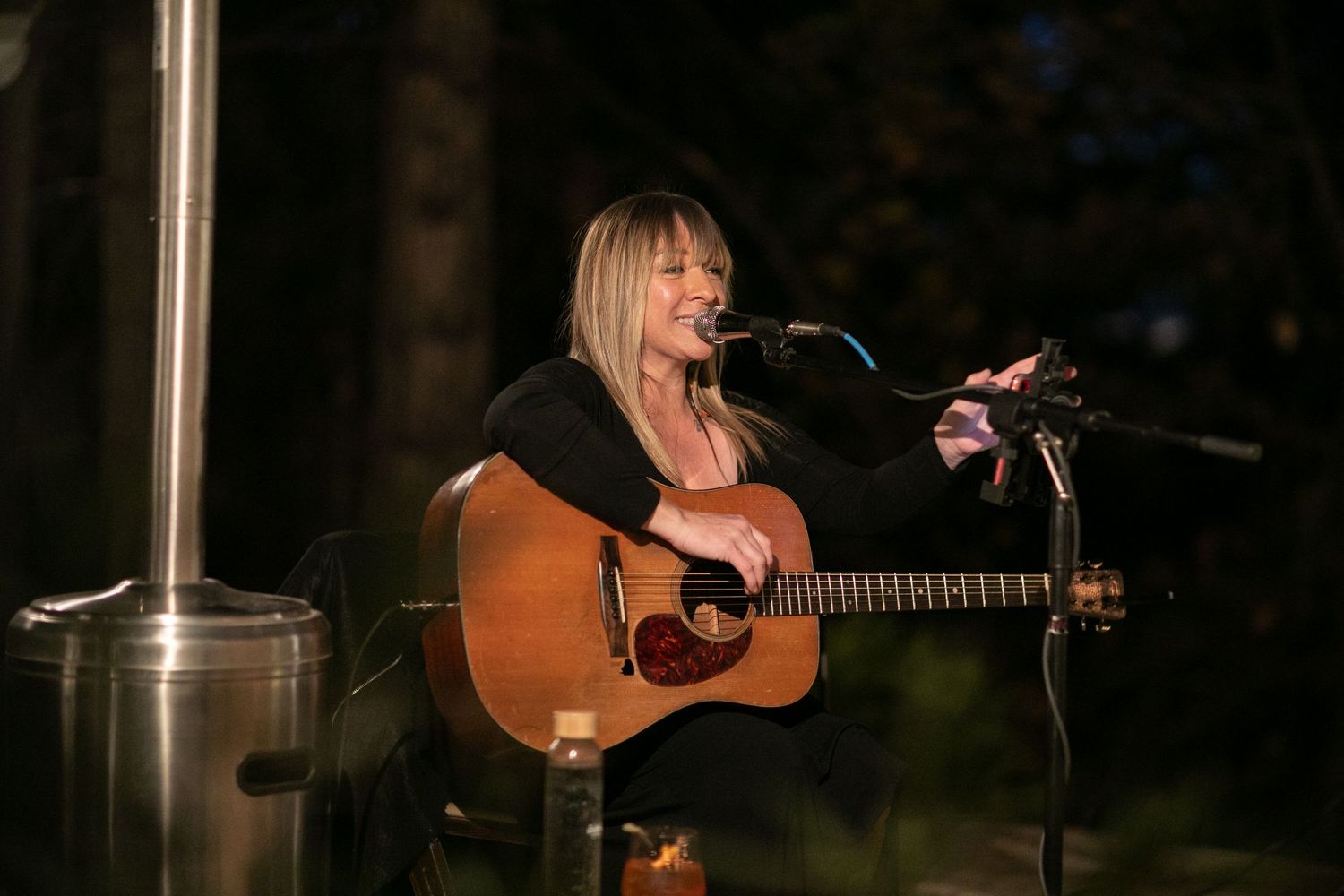 Acoustic performance at night with warm lighting and natural forest backdrop.