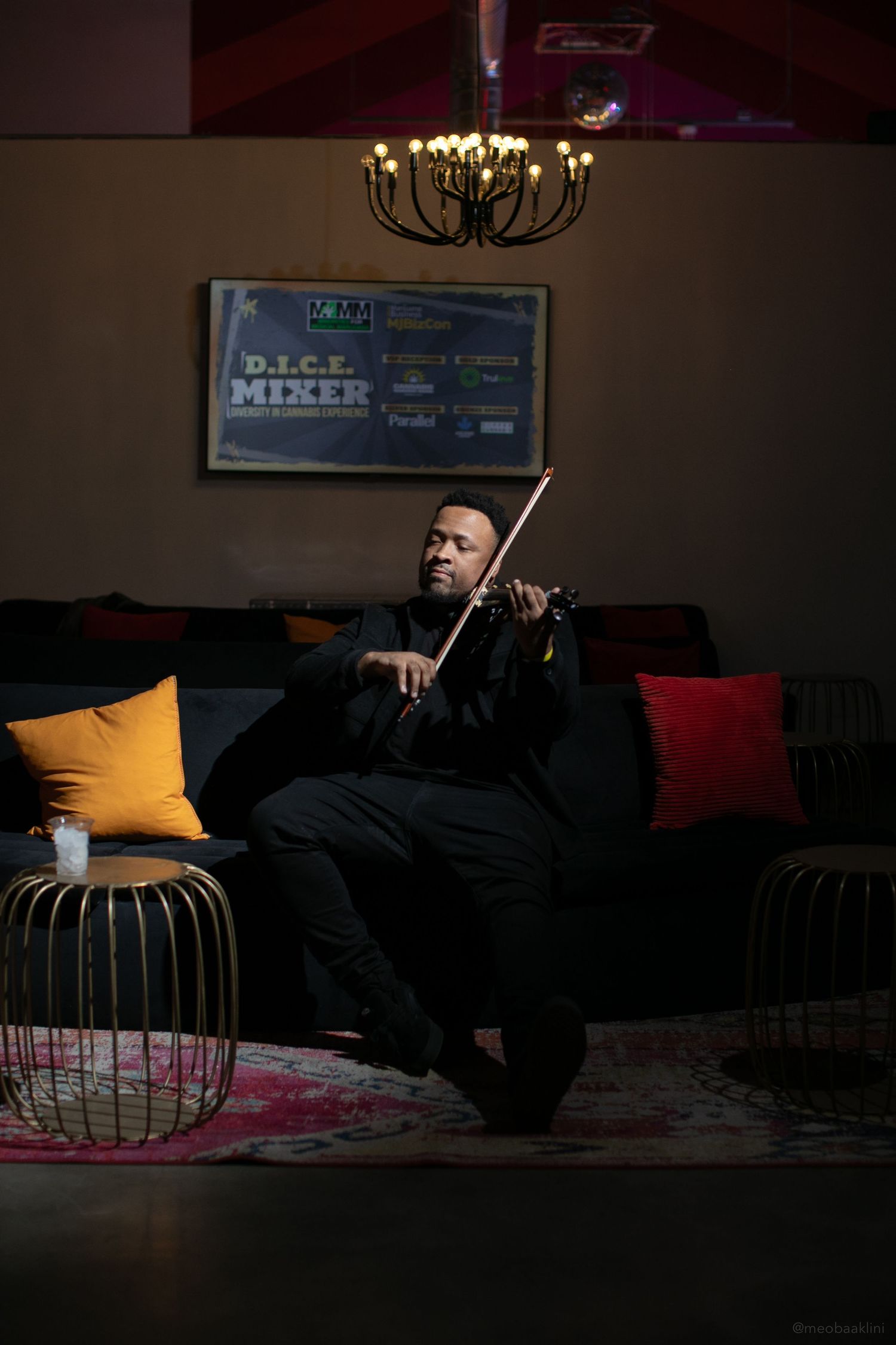 Person lounging on a dark couch in a dimly lit room with event signage visible.