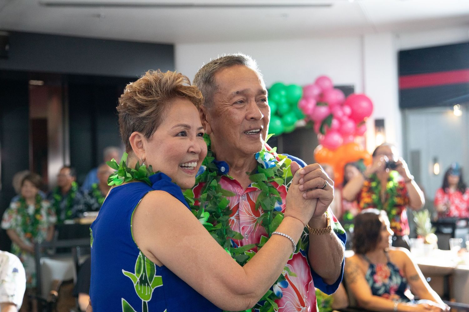 People in matching tropical print outfits dancing together at celebration.